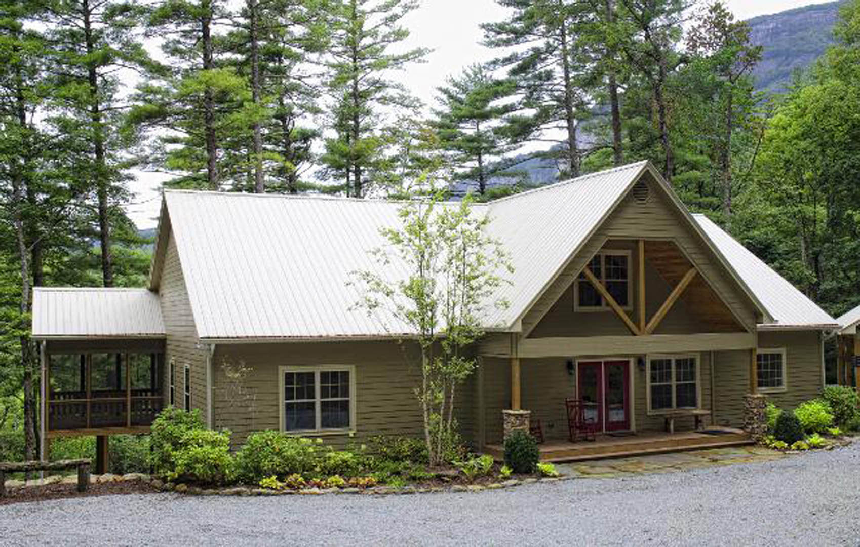 White-roofed cottage with white front door, grid window, and leafy tree beside porch