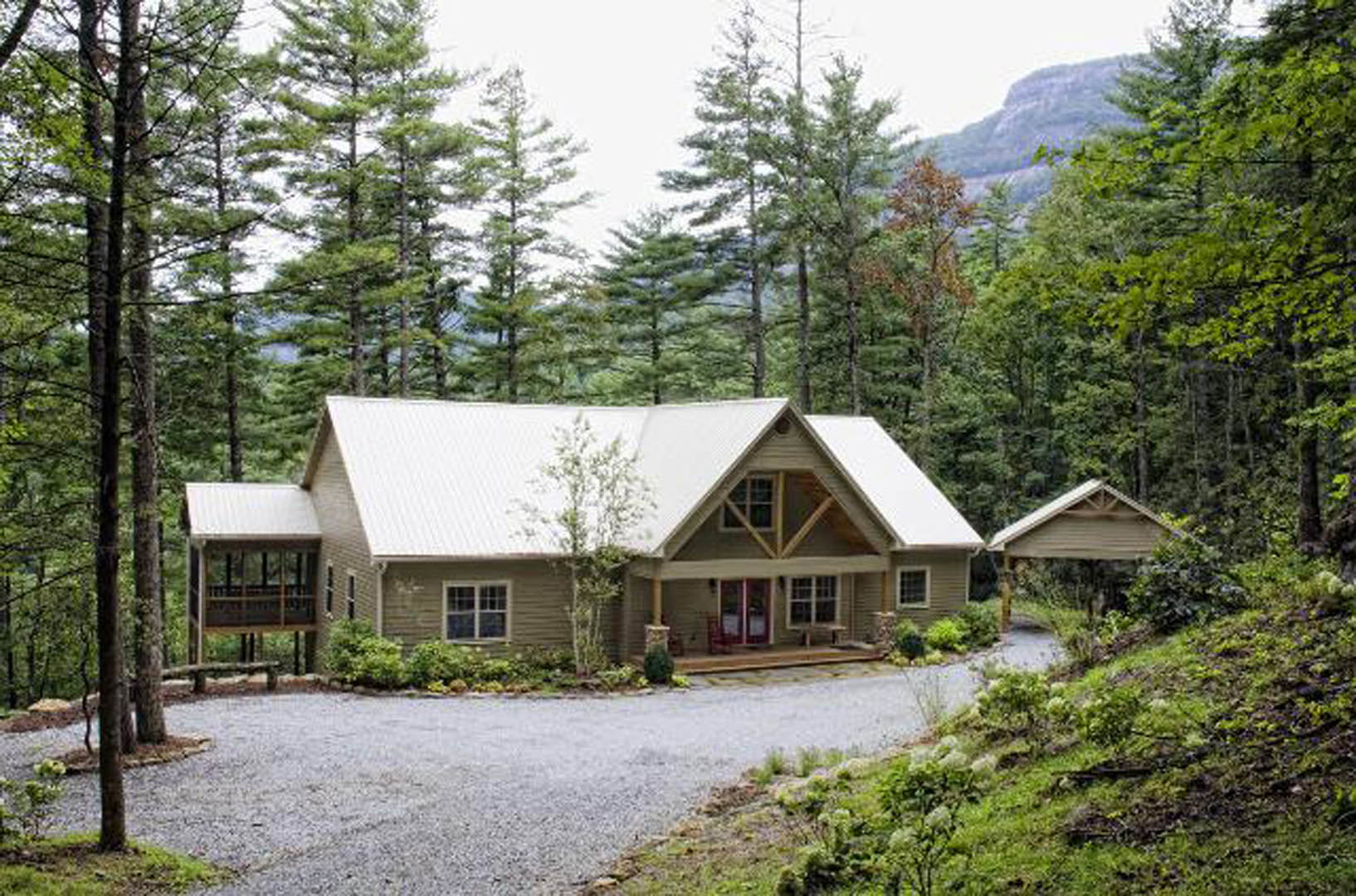 Two-story house with white siding, multi-pane windows, covered front porch, paved driveway, mature trees and shrubs in landscaped yard