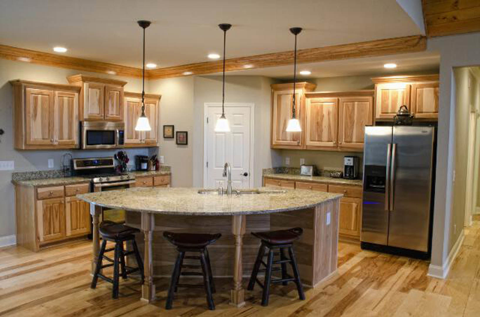 Spacious kitchen featuring a large central island with bar stools, stainless steel refrigerator, white cabinetry, stone countertops, and hardwood flooring