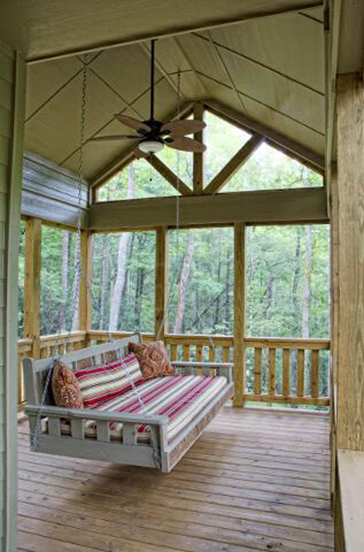 Covered porch with wooden bench topped with pillows, wood flooring, ceiling fan above, and neutral walls.