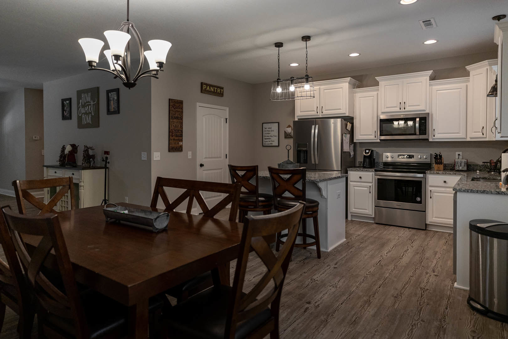 Open kitchen and dining area featuring wood cabinetry, stainless steel oven with black cooktop, microwave, rectangular dining table with metal tray, upholstered chairs, whiteboard