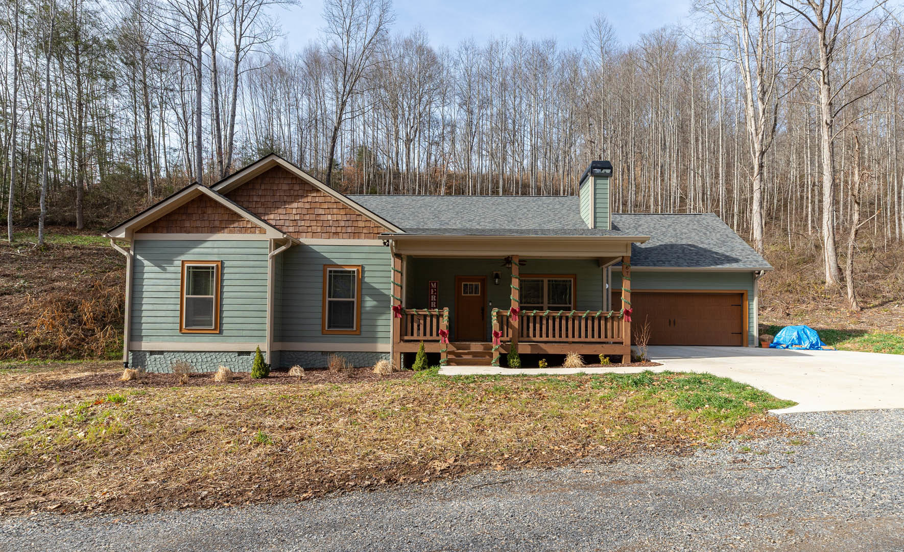 Two-story house with white siding, attached garage, concrete driveway, screened window with white frame, blue tarp on ground, gravel road bordered by grass and dirt, covered front