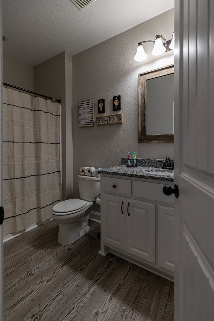 Modern bathroom with white tile walls, a sleek toilet, rectangular sink on a stone countertop, chrome faucet, and a two-bulb light fixture above a large mirror.