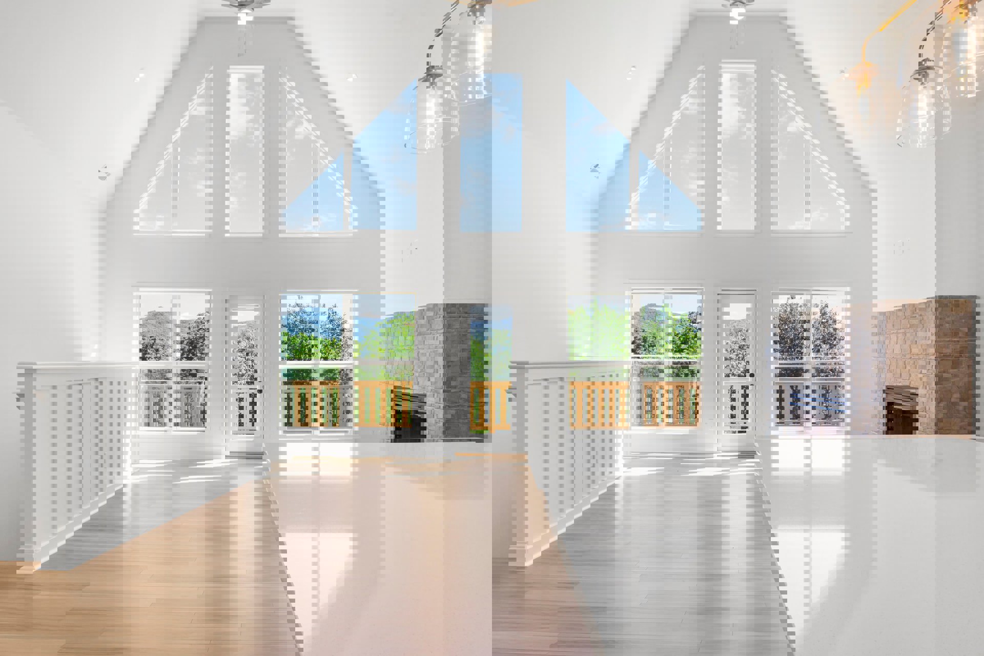 Open kitchen with expansive white countertop, wood flooring, clear glass dome pendant lights, white walls, and large windows showing blue sky
