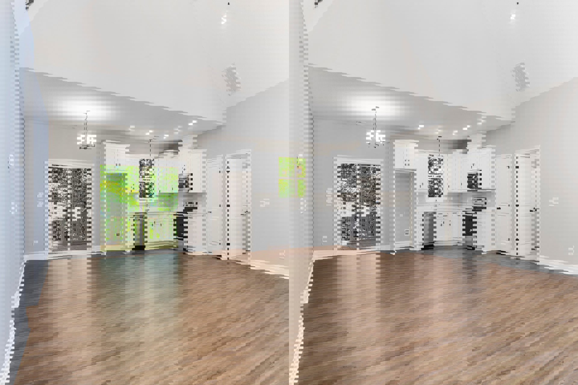 Spacious kitchen with white cabinetry, hardwood flooring, sliding glass door overlooking trees, built-in microwave, and white door with black handles