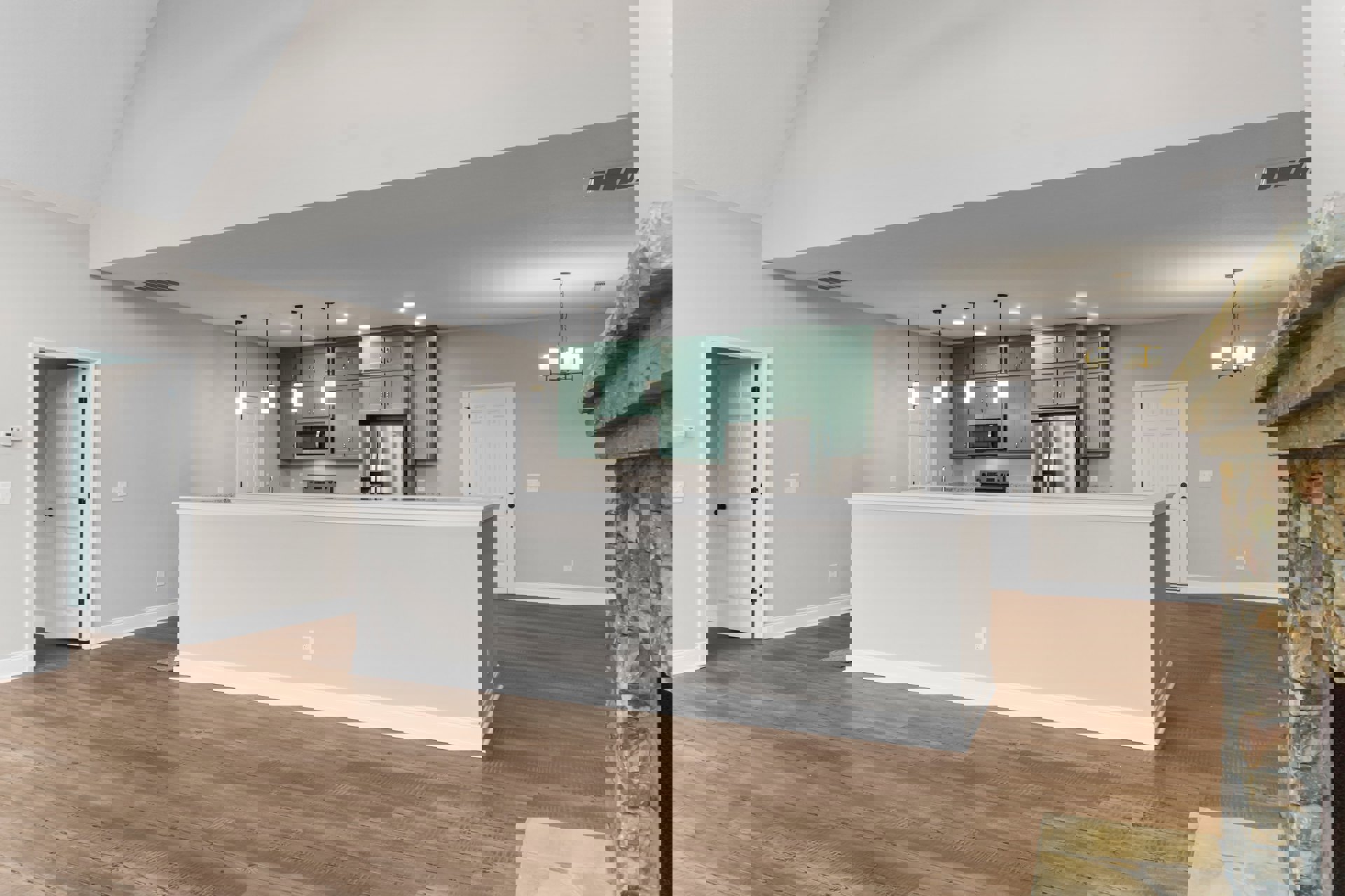 Open kitchen and dining area featuring stainless steel stove and refrigerator, white cabinetry with black hardware, wood laminate flooring, white walls, and a microwave oven.