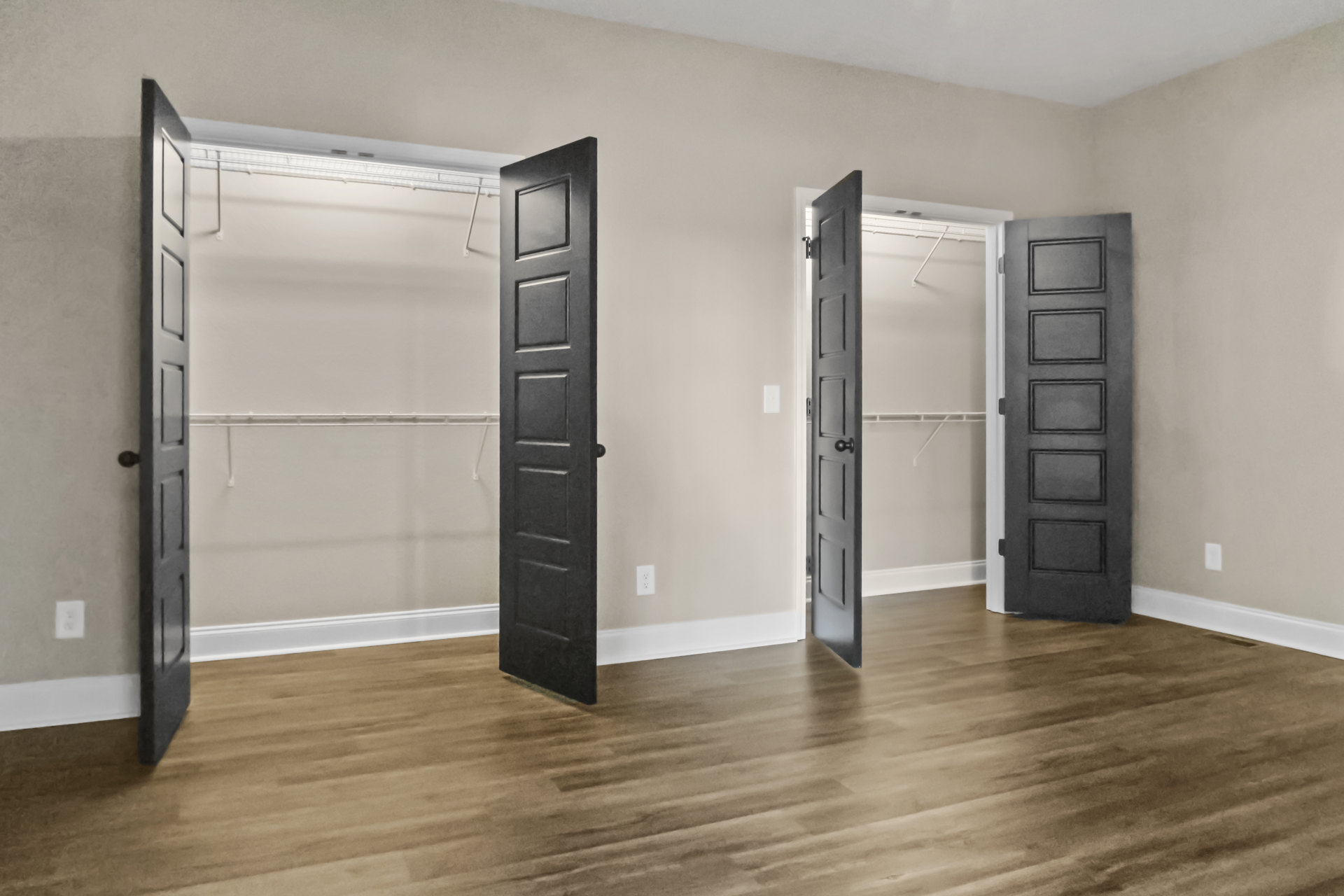 Wood floor leads to a room with open black doors, revealing clothes racks and a black cabinet with square paneling against white walls.