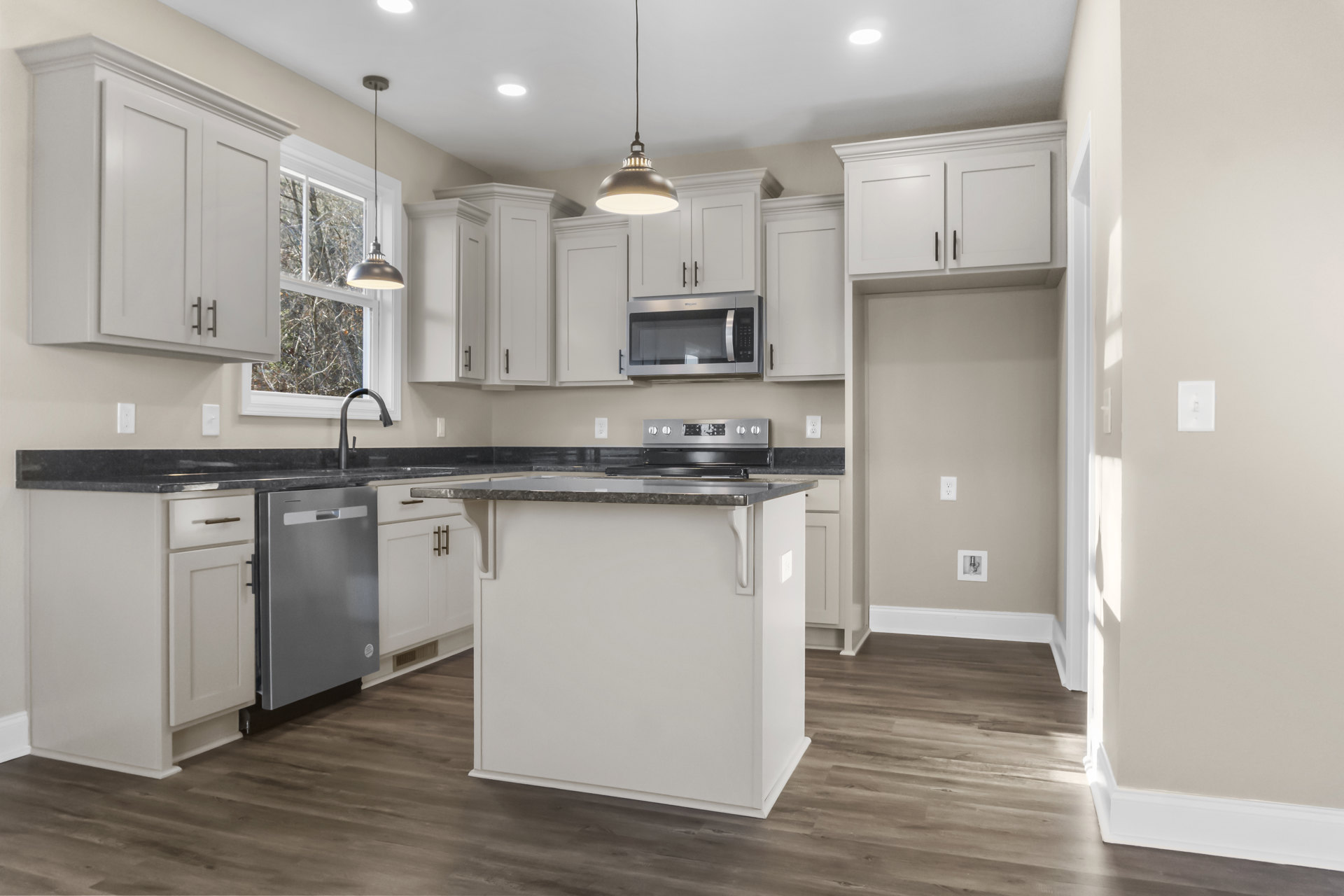 Spacious kitchen featuring a white island with black countertop, stainless steel dishwasher, glass door microwave, modern pendant light, light switch on wall, and close-up of