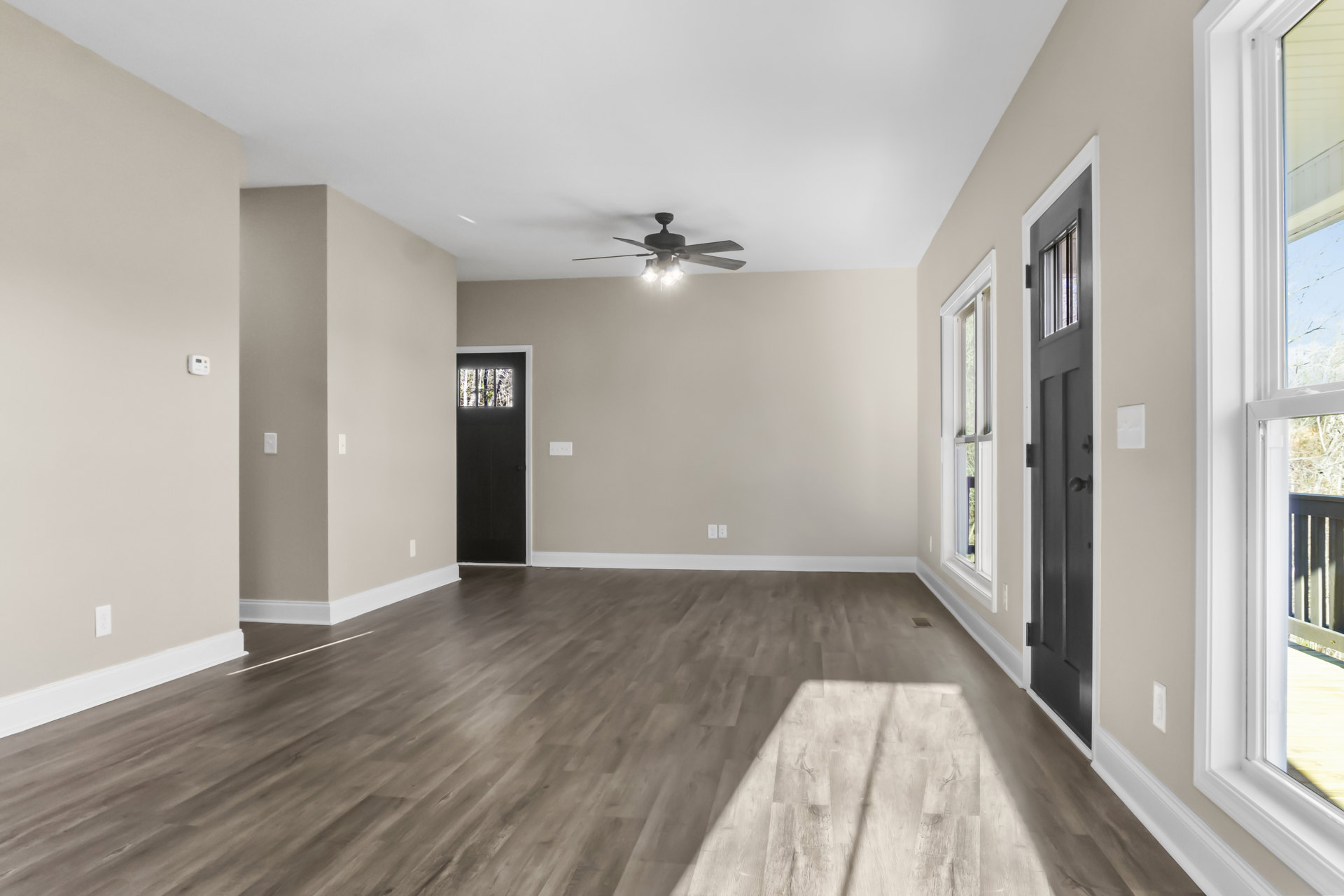 Ceiling fan with lights above wood laminate flooring, black door with frosted glass and silver knob, window overlooking outdoor deck, white plaster walls