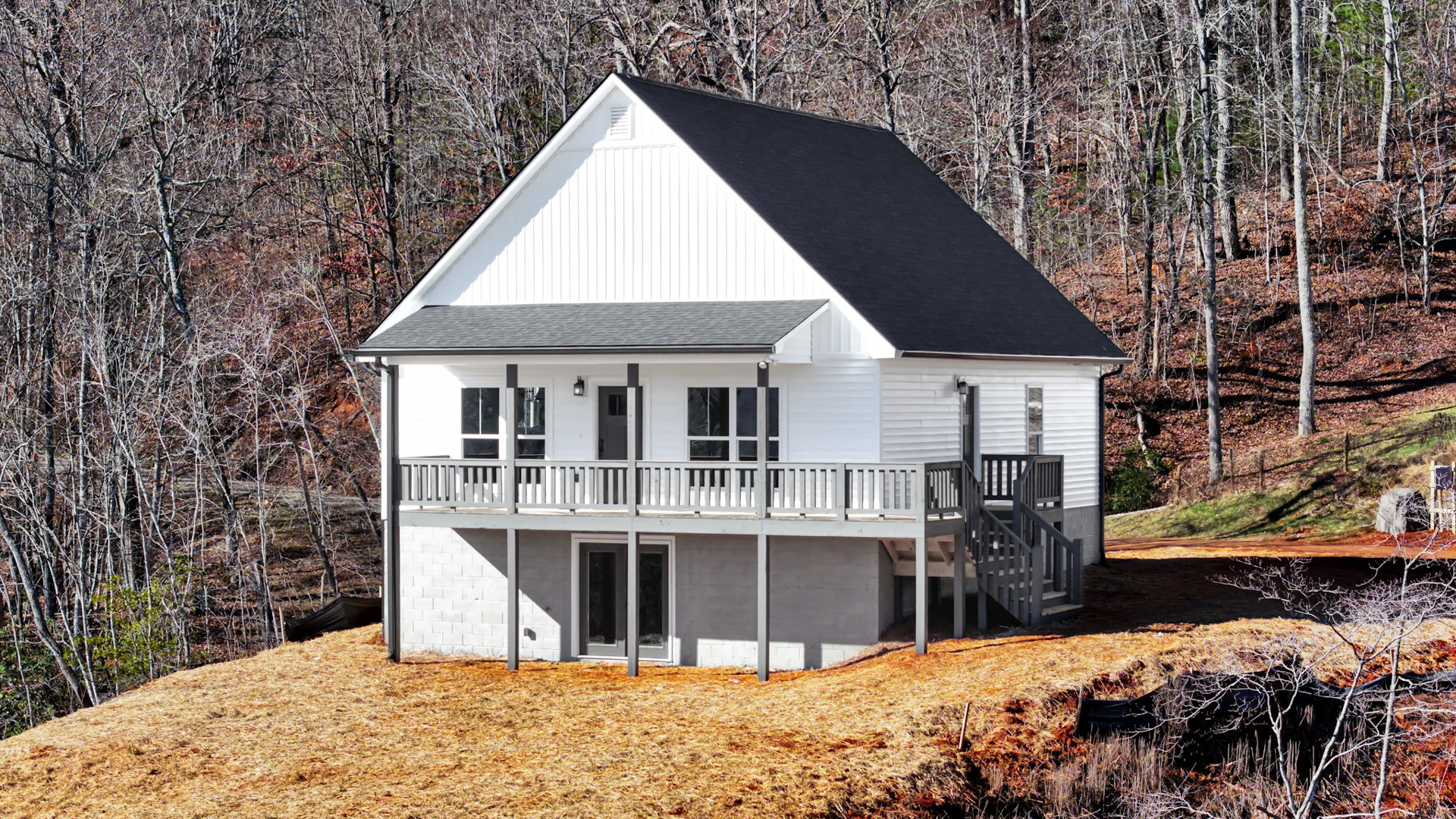 Two-story house with white siding, large windows, covered front porch, and wooden deck overlooking a grassy lawn with mature trees