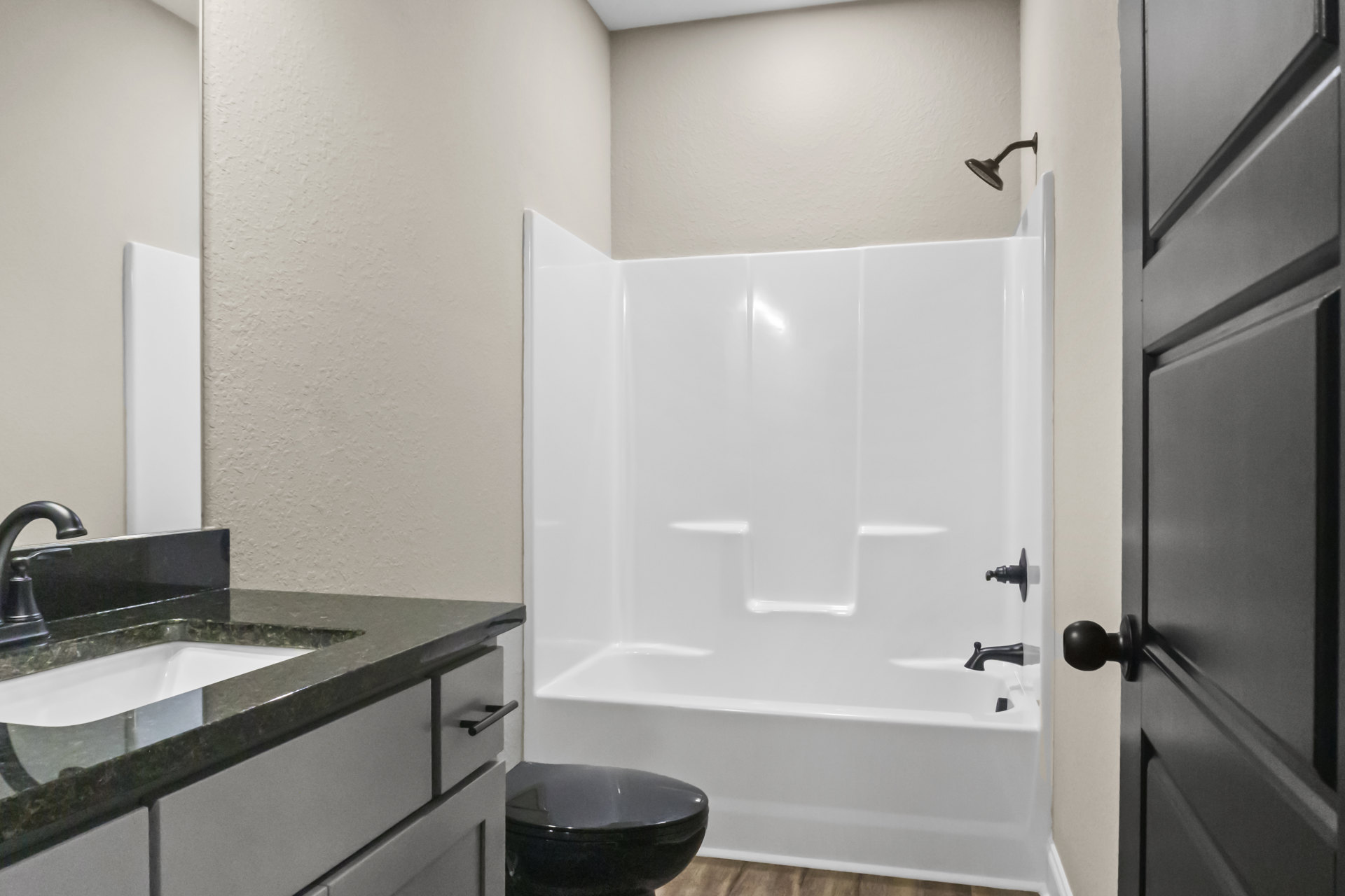 Modern bathroom featuring a glass-enclosed shower, white freestanding bathtub, black toilet bowl against a white tiled wall, sleek sink with chrome faucet, light wood cabinetry