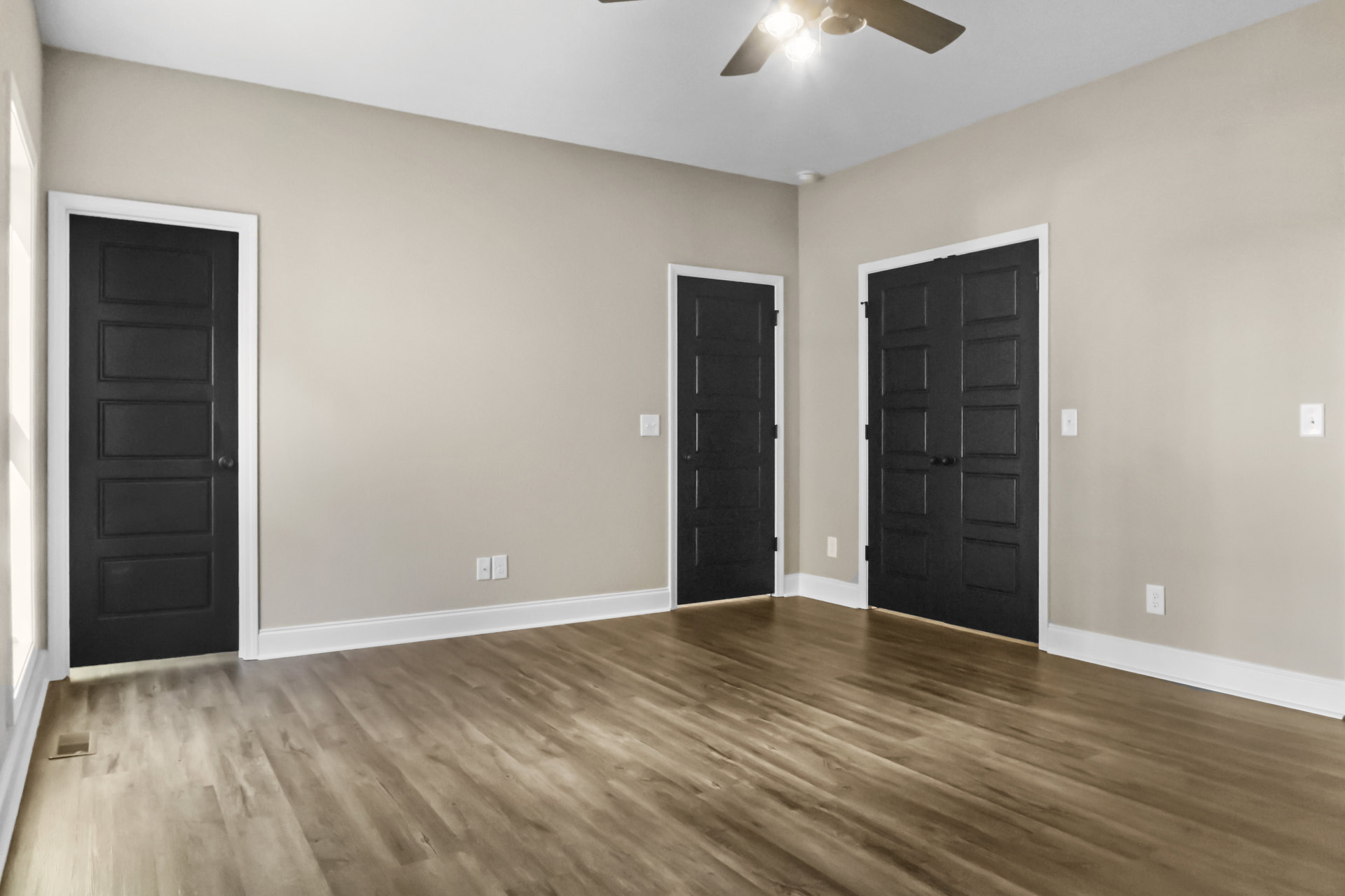 Room with black paneled doors, white trim, wood flooring, and a ceiling fan with light fixture