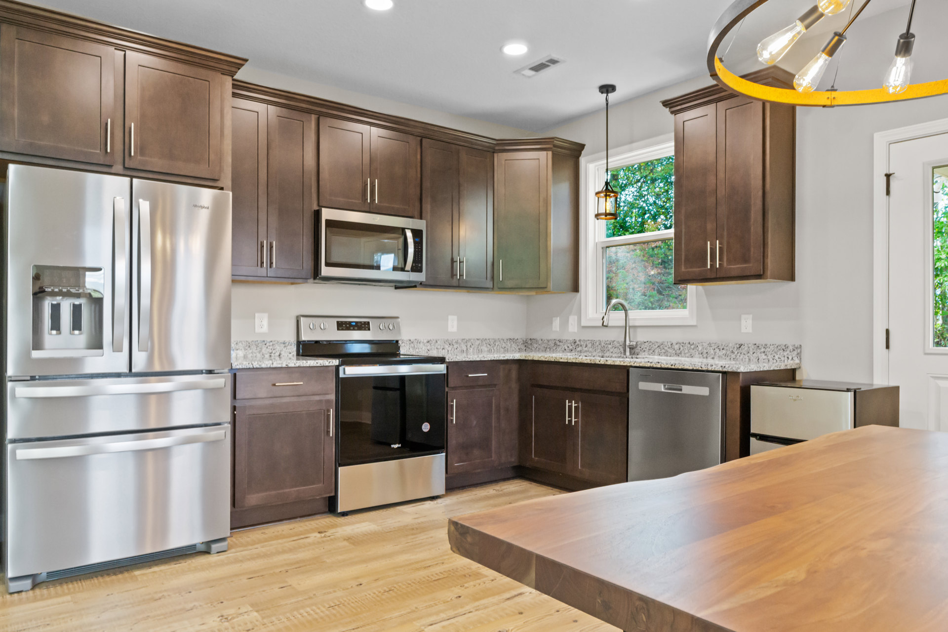 Kitchen with dark wood cabinets, stainless steel refrigerator, built-in microwave, glass door stove, wooden dining table, and overhead light bulb