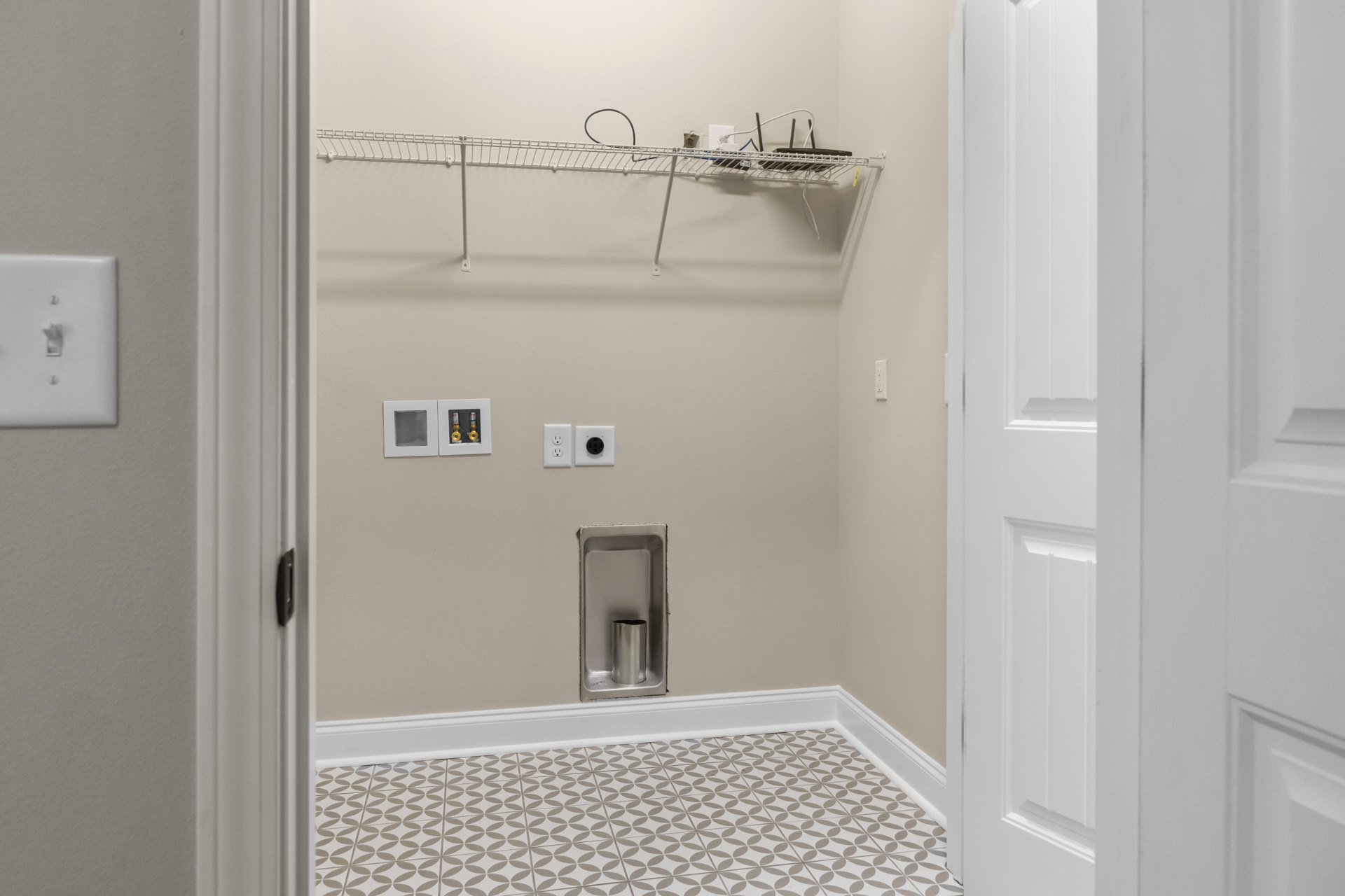Bathroom with white door, built-in shelf, tile flooring, white baseboards, silver plumbing fixture on wall, light switch, white storage boxes containing yellow and gold items