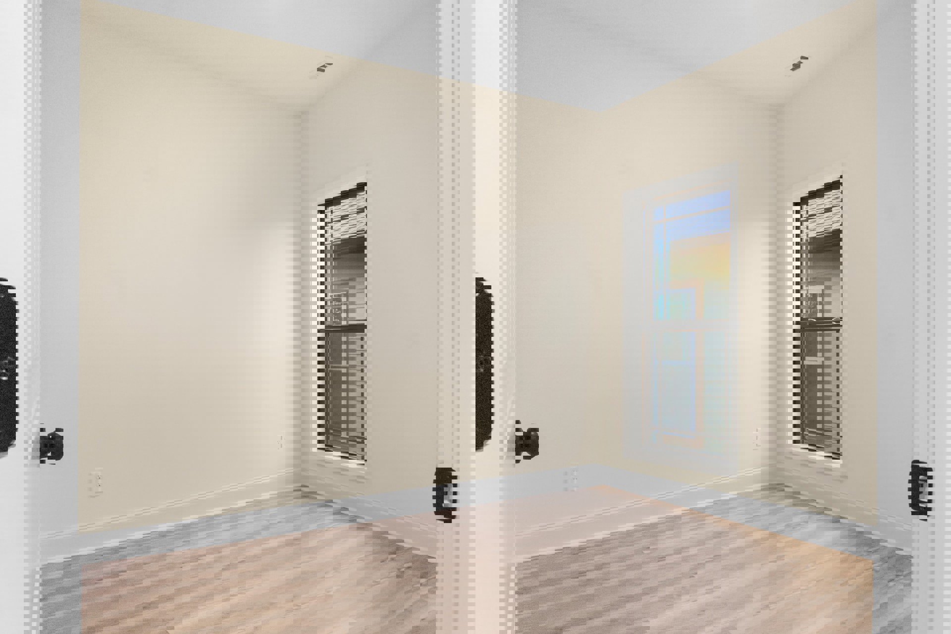 Sunlit room featuring wide-plank hardwood flooring, white baseboards, smooth plaster walls, and a large window with minimalist trim.