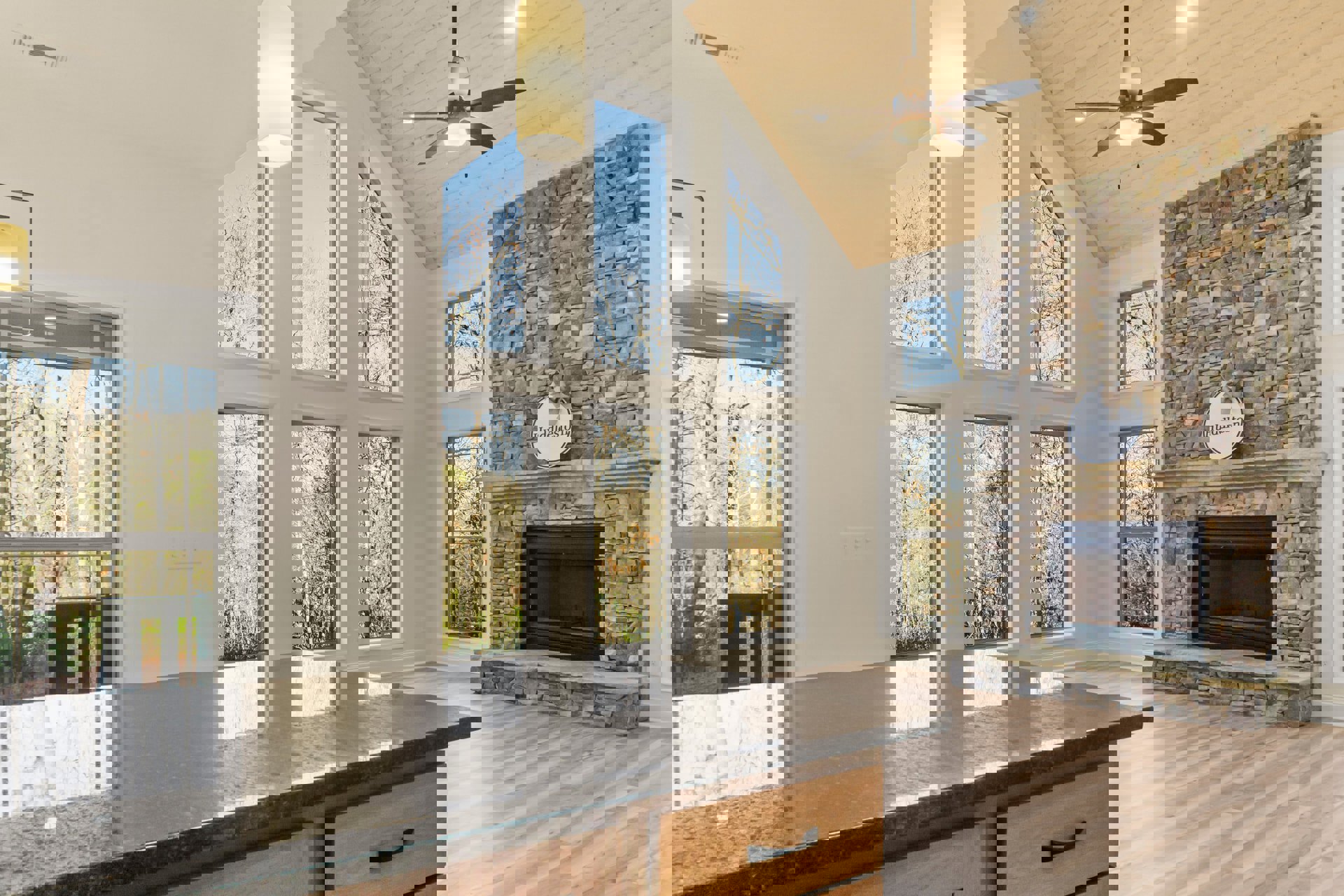 Living room with stone fireplace, glass door insert, wood flooring, ceiling fan with light, and neutral walls