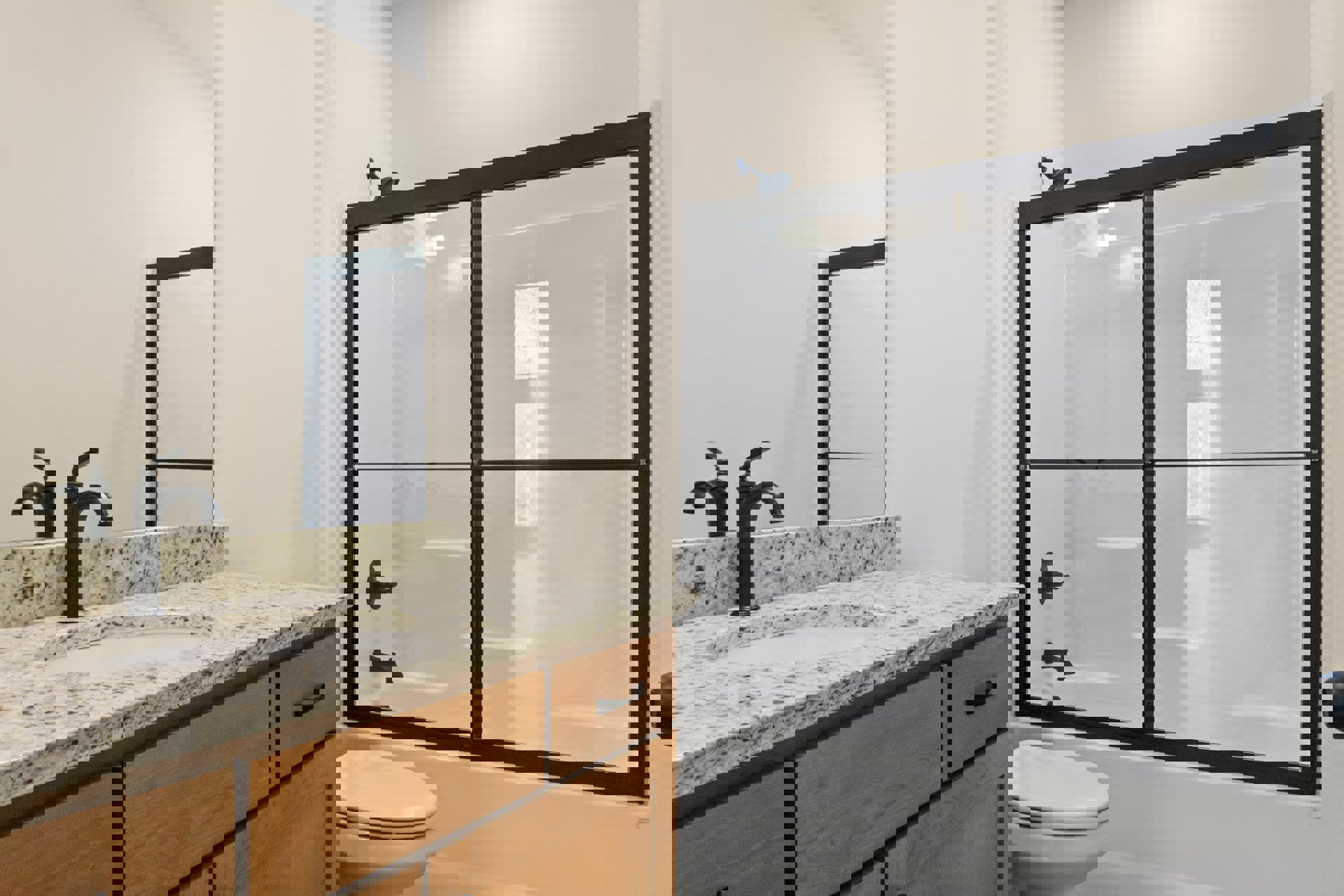 Modern bathroom featuring a glass-enclosed shower, white porcelain sink set in a wood vanity with storage cabinets, chrome faucet, and a toilet with closed lid; neutral tile walls