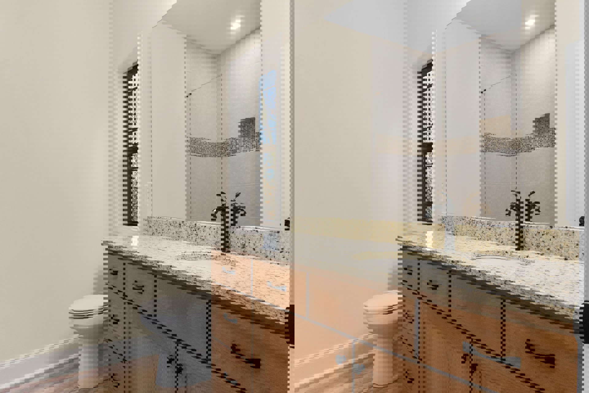 Modern bathroom featuring a white toilet, wood vanity with integrated sink, chrome faucet, large mirror, and light tile flooring