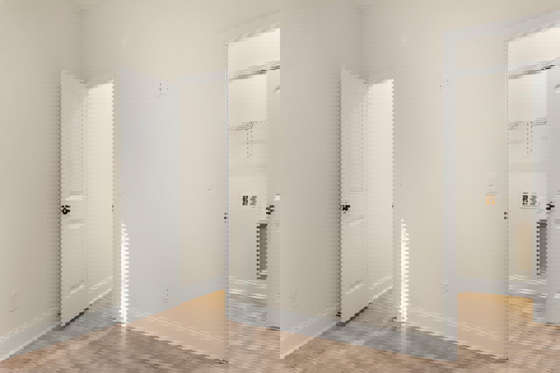 Open white door leading into a room with wood flooring and white baseboards, white walls featuring electrical outlets, and a silver door handle.