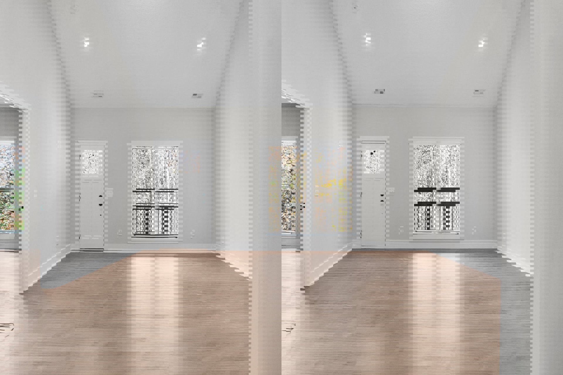 Hardwood floor room with white walls, white door featuring glass window, large window overlooking trees, sunlight illuminating floor