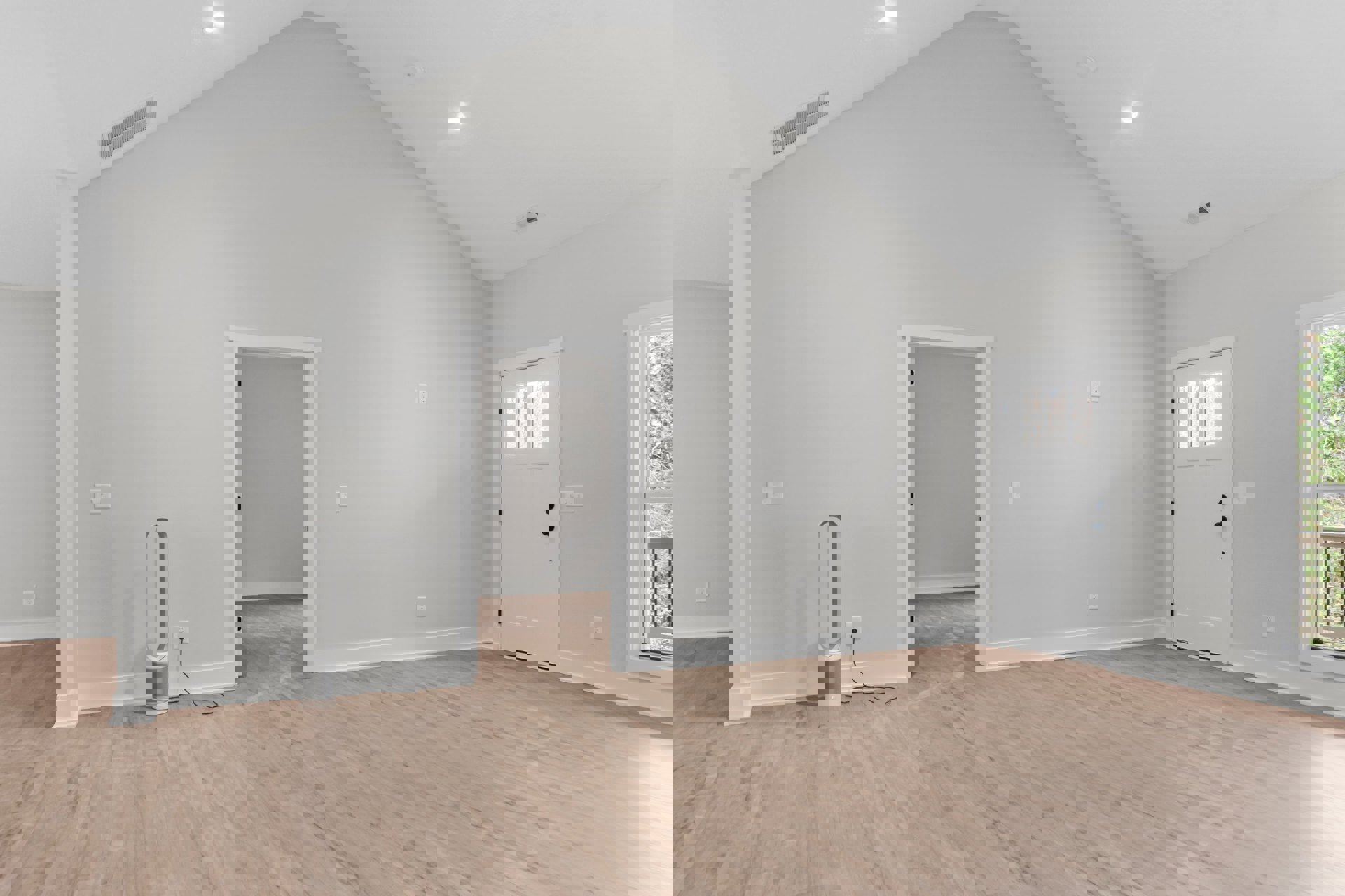 Wood flooring and white walls in a bright room, featuring a white door with glass panes, a window overlooking trees, and a floor vent.
