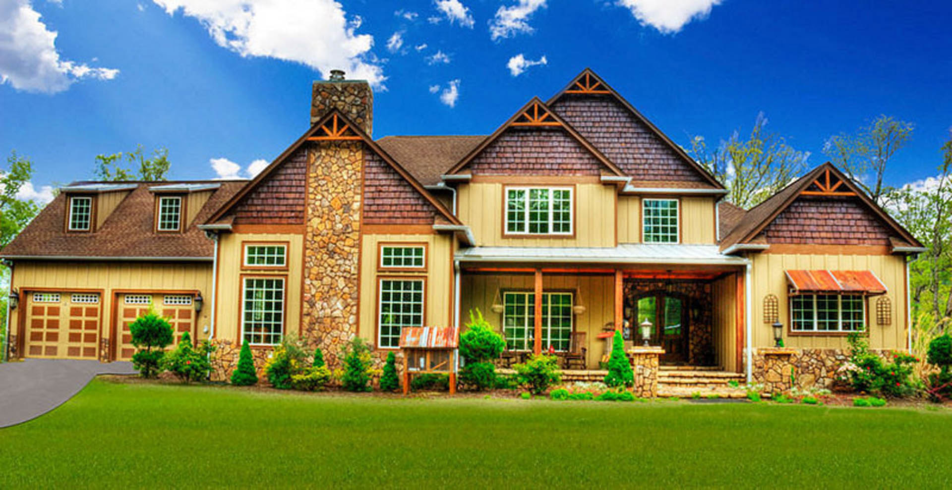 Two-story house with white siding, dark roof, grid windows, manicured green lawn, shrubs, and blue sky with scattered clouds