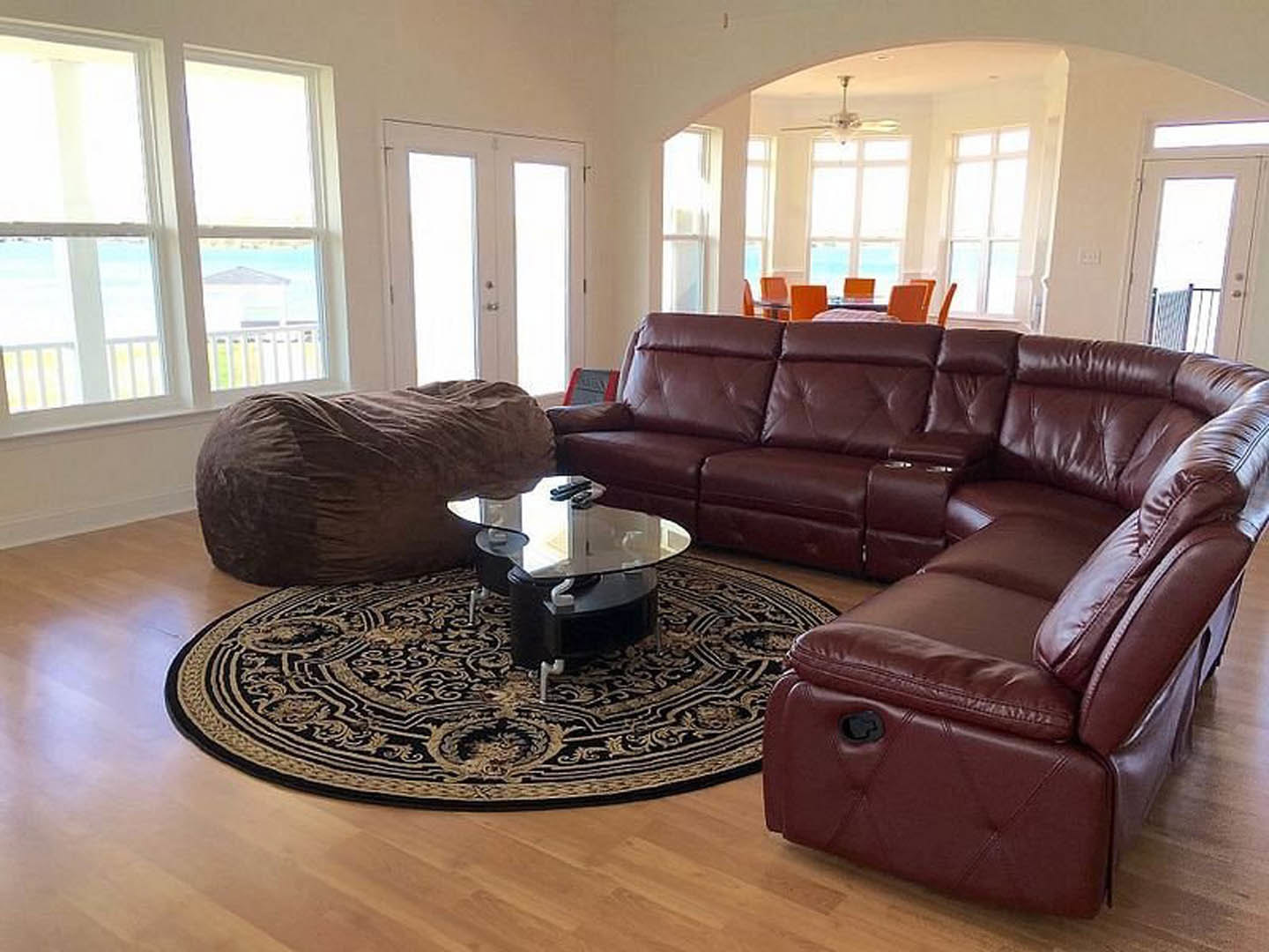 Living room with a gray couch, round patterned rug, glass coffee table, brown bean bag chair, and double glass-paneled doors