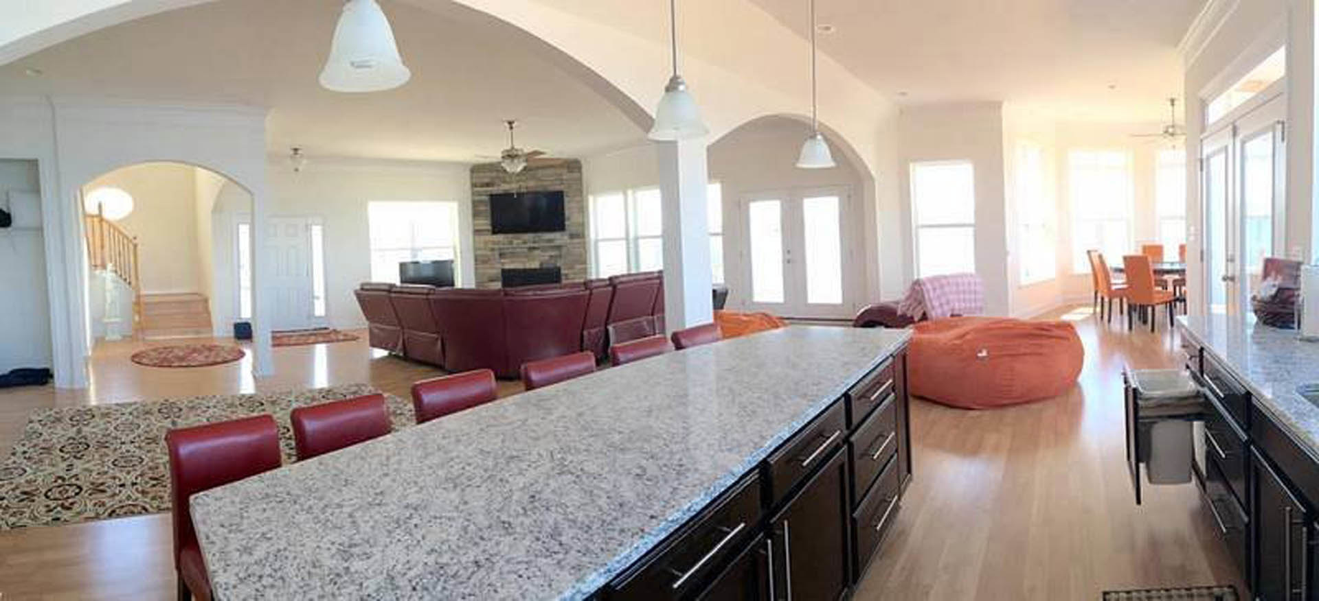 Spacious kitchen with wood cabinetry, stone countertops, large dining table surrounded by chairs, light flooring, and windows along the back wall