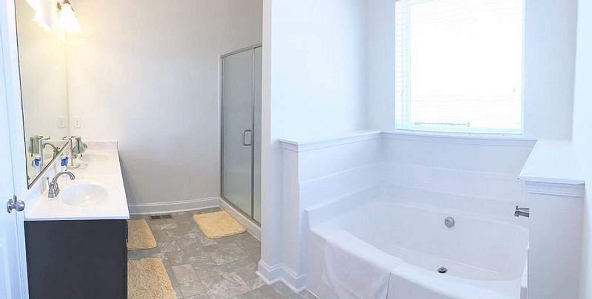 Modern bathroom featuring a freestanding bathtub, glass-enclosed shower with tiled walls, white vanity with undermount sink, chrome faucet, and neutral tile flooring