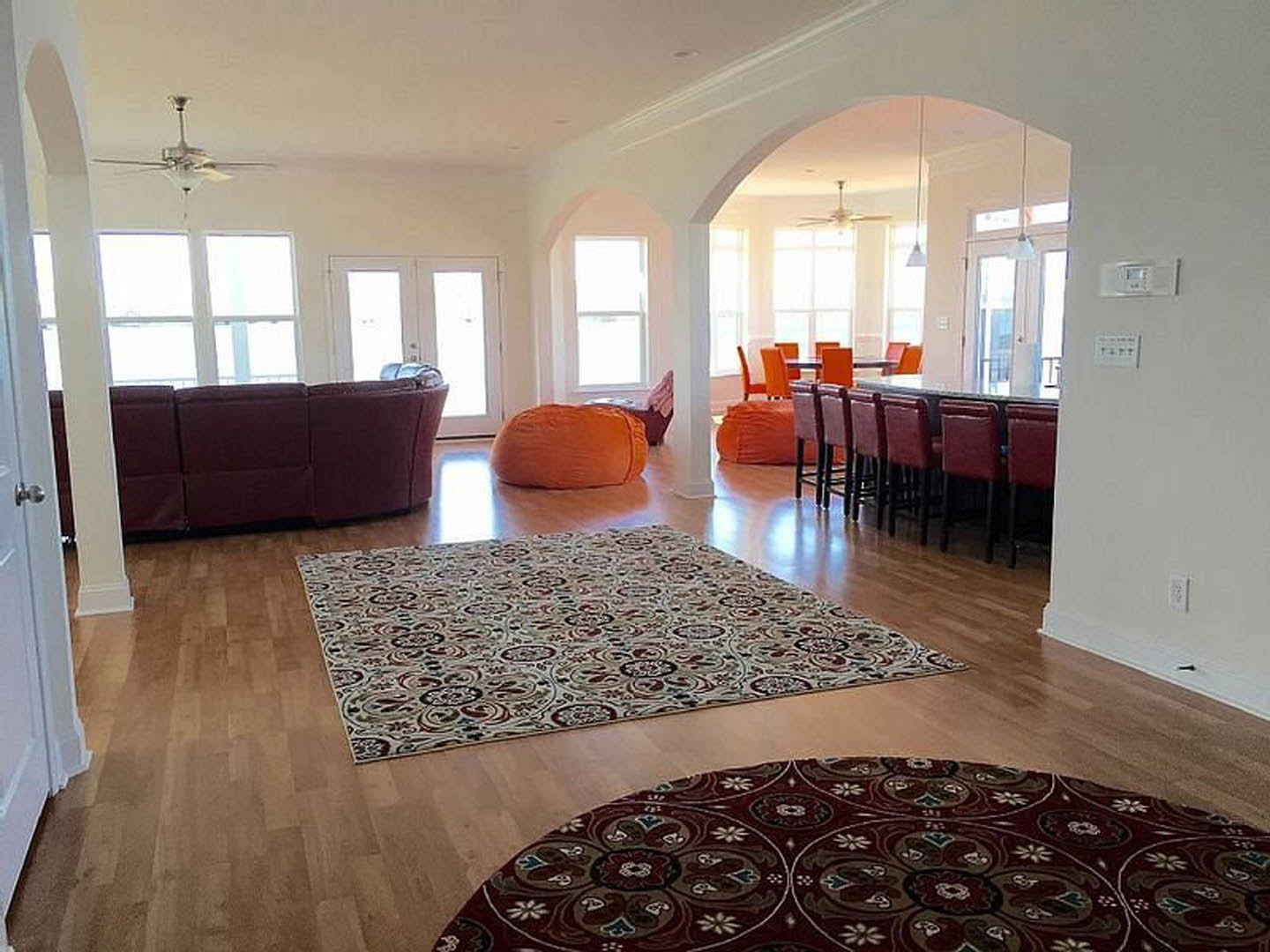 Spacious living room featuring a patterned area rug on wood flooring, two upholstered couches with accent pillows, neutral walls, and a flat-screen television
