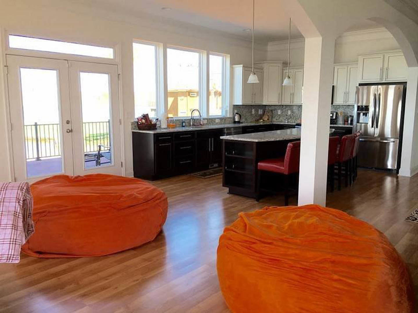 Two large orange bean bags on a wood floor in an open room with a modern kitchen, dining area, and white cabinetry