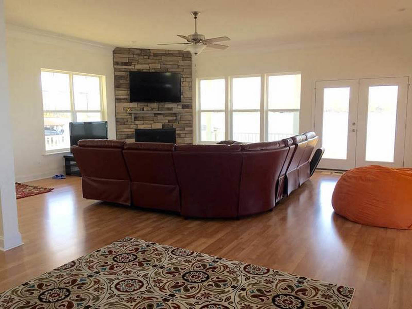 Living room with gray couch, brick fireplace, wall-mounted TV, light laminate flooring, and textured area rug