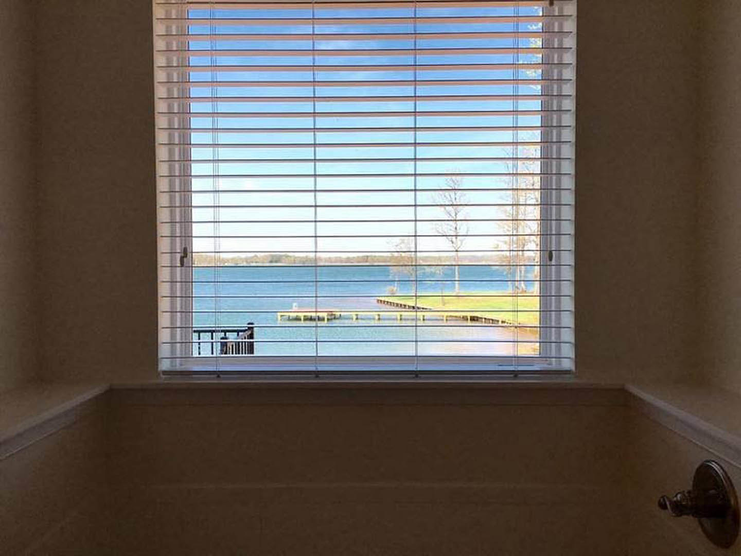 Large window with white horizontal blinds set in a light-colored wall, sunlight filtering through slats, interior residential space