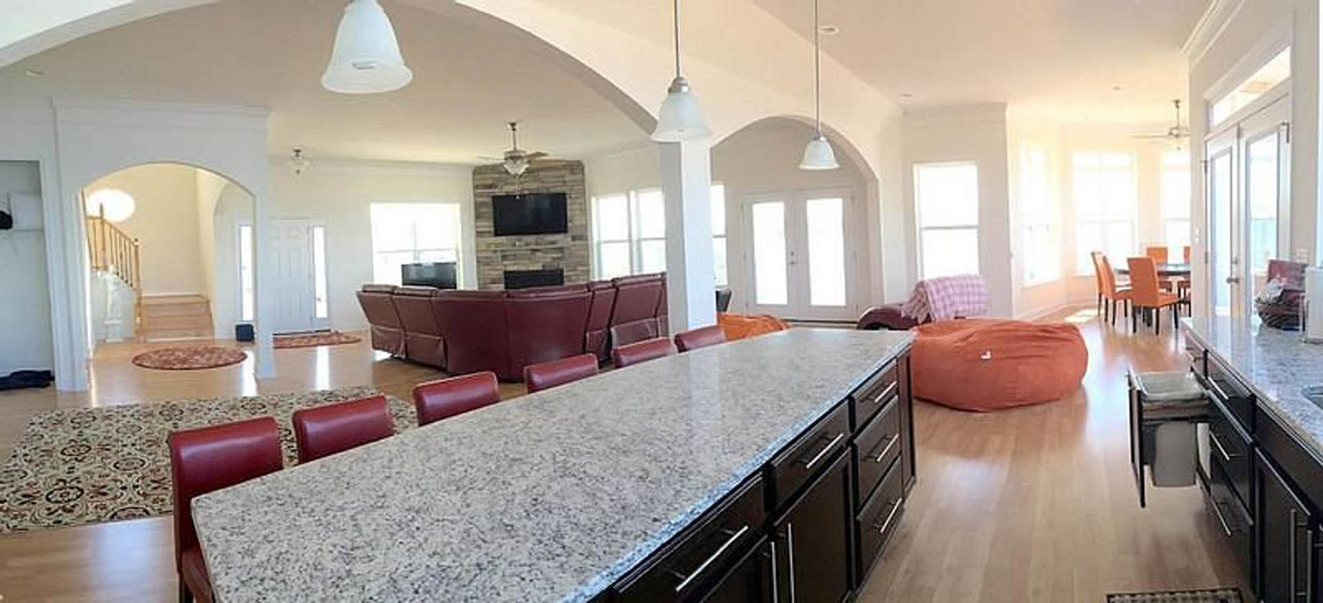 Spacious kitchen featuring light wood cabinetry, stone countertops, large dining table with chairs, hardwood flooring, and tall windows providing natural light