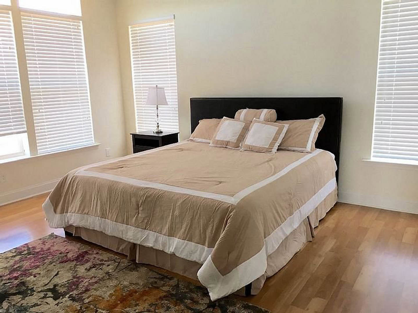 Neutral-toned bedroom with upholstered bed, layered pillows, bedside table, modern lamp, and white window shade