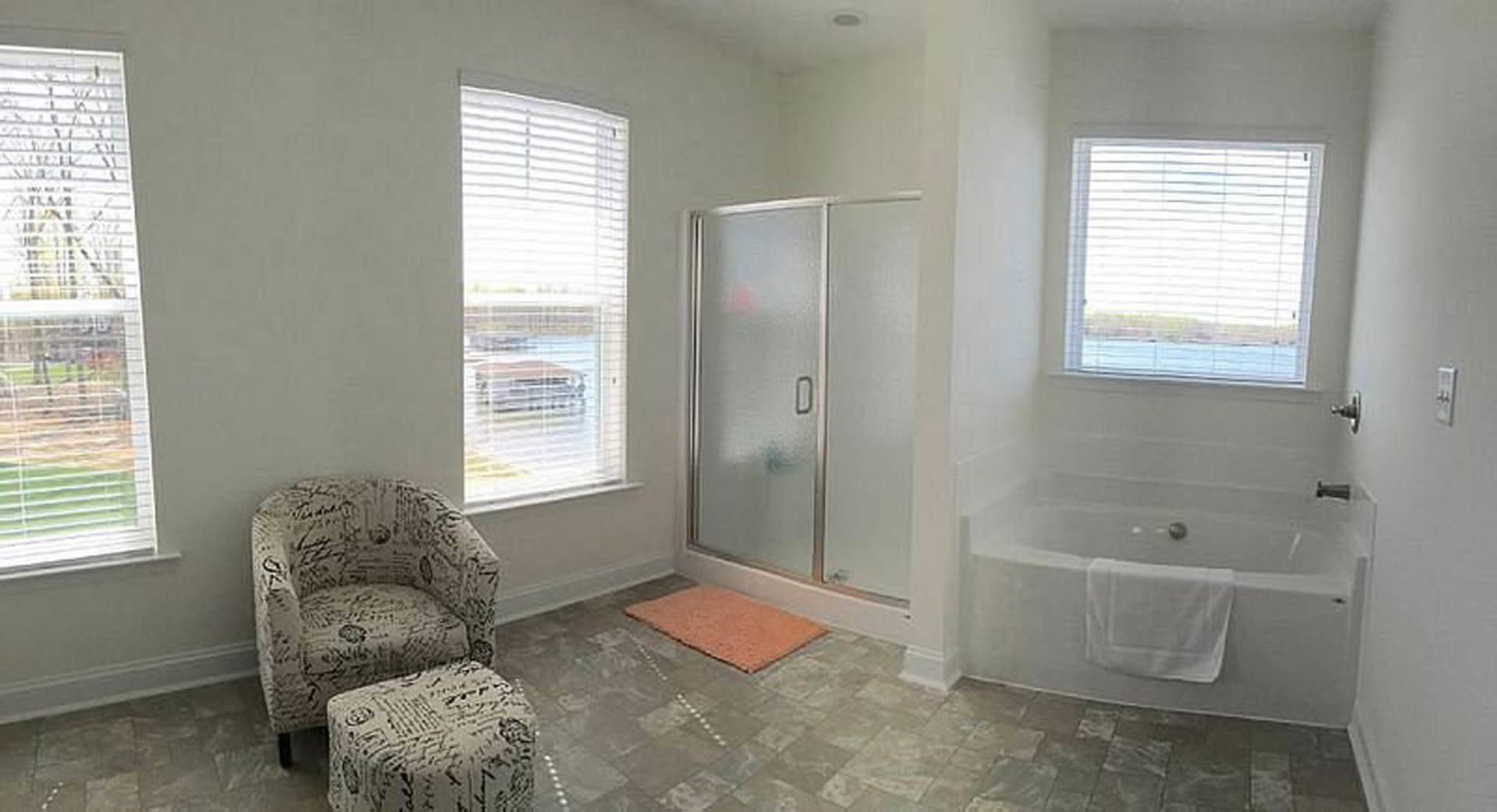 Modern bathroom featuring a freestanding bathtub, glass-enclosed shower with tile walls, large window, neutral flooring, and a white towel folded on a vanity.