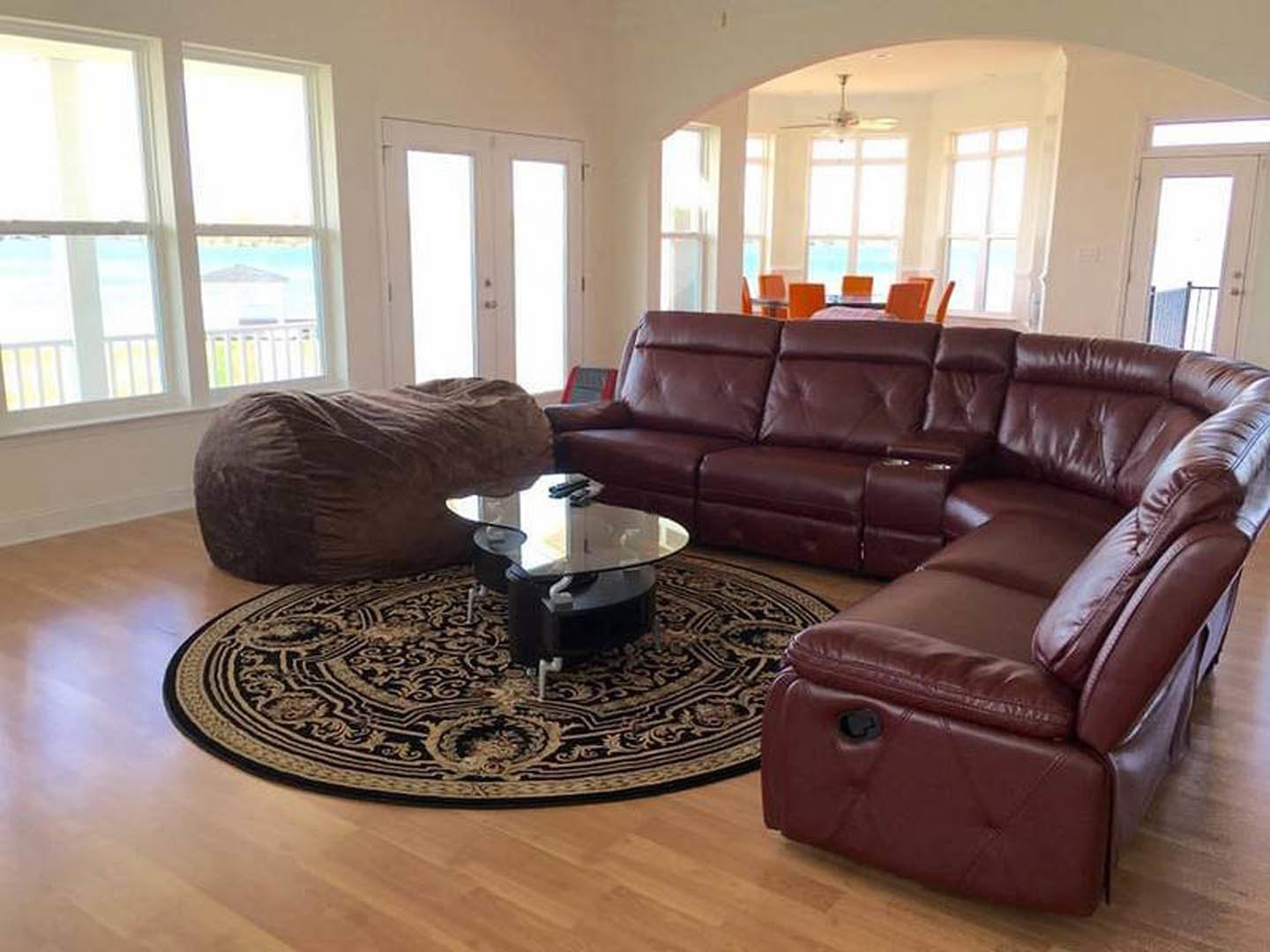 Living room with light gray couch, round woven rug, glass coffee table, brown throw blanket, white walls, hardwood flooring
