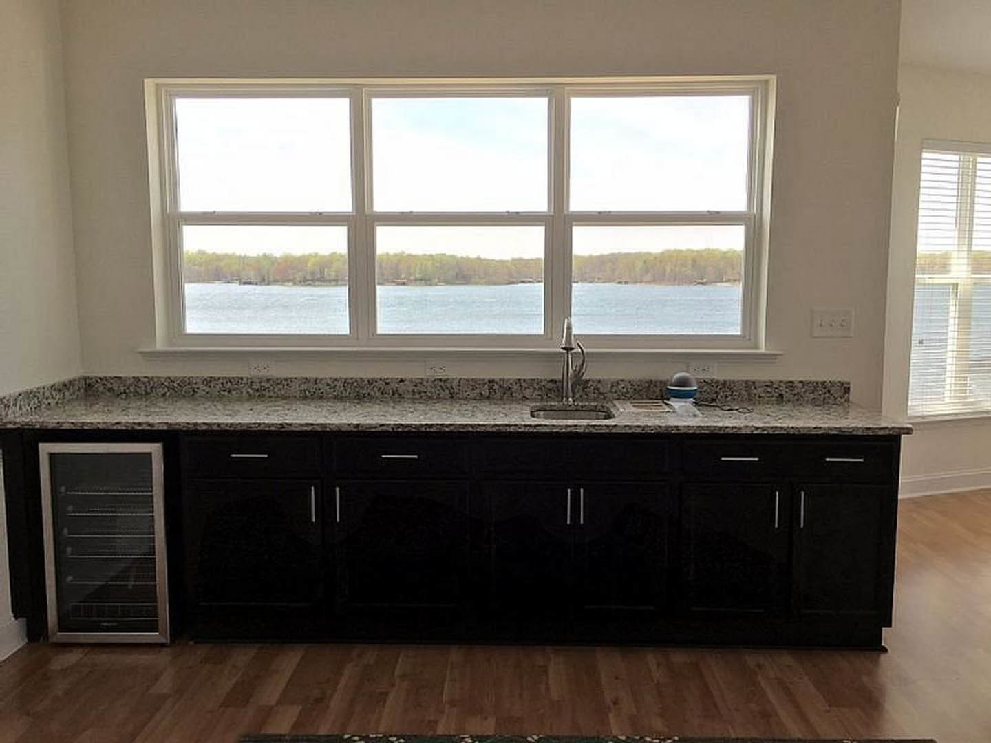 Modern kitchen featuring a large window overlooking water, white cabinetry, stone countertops, stainless steel sink, and hardwood flooring