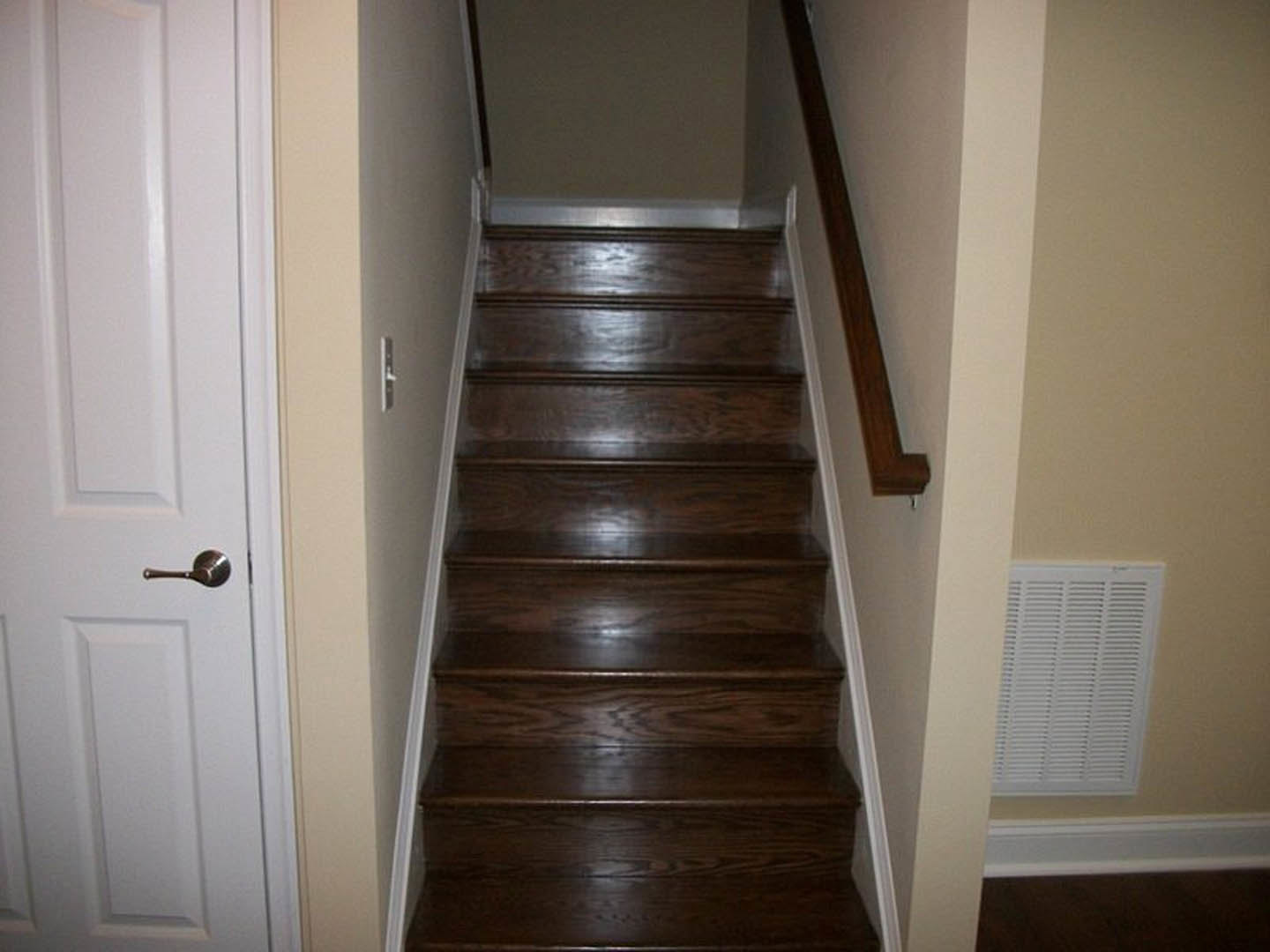 Wooden staircase with varnished hardwood steps, white wall vent, close-up views of wood plank flooring, metal pipe, and brushed metal door handle