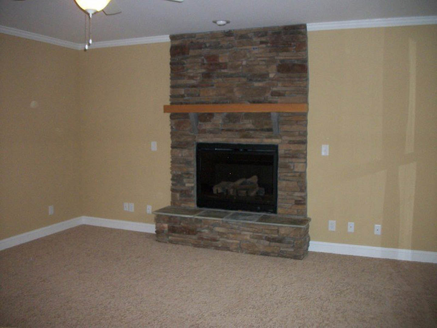 Stone fireplace with stacked wood logs, brick wall surround, carpeted floor, and metal fire screen in a cozy den.