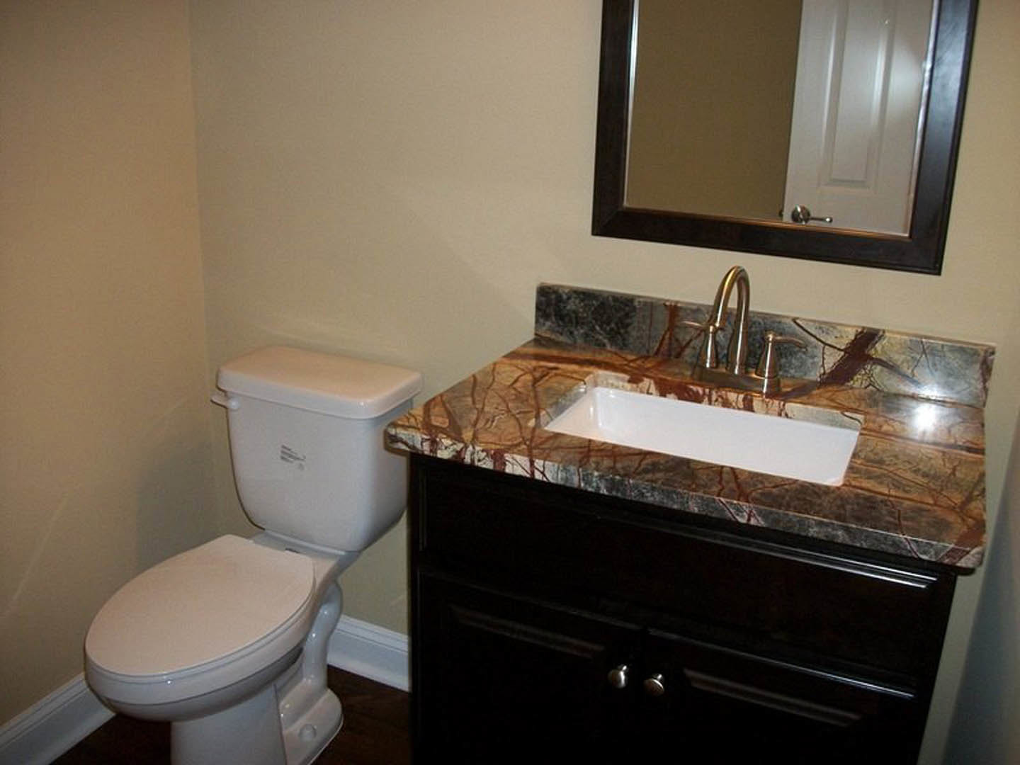 Marble countertop vanity with undermount sink, chrome faucet, large framed mirror, white toilet, light gray tile flooring, and neutral wall paint