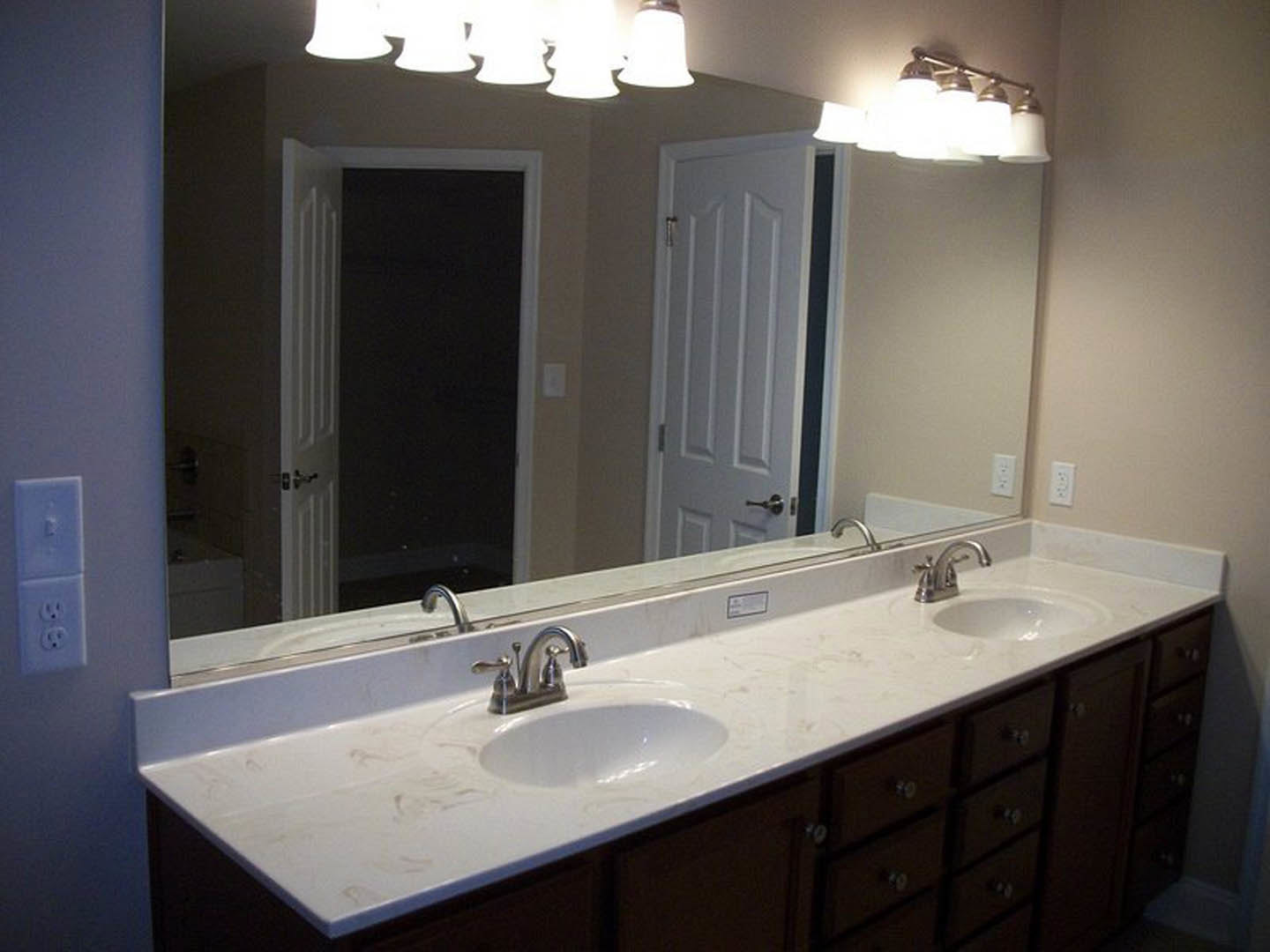 Bathroom with a wide mirror above a white sink, chrome faucet, tiled backsplash, and white electrical outlet on the wall