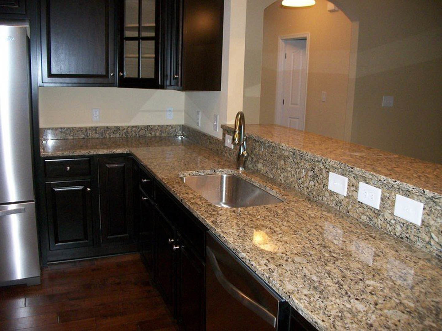 Granite kitchen countertops with stainless steel sink, chrome faucet, white tile backsplash, and wood cabinetry