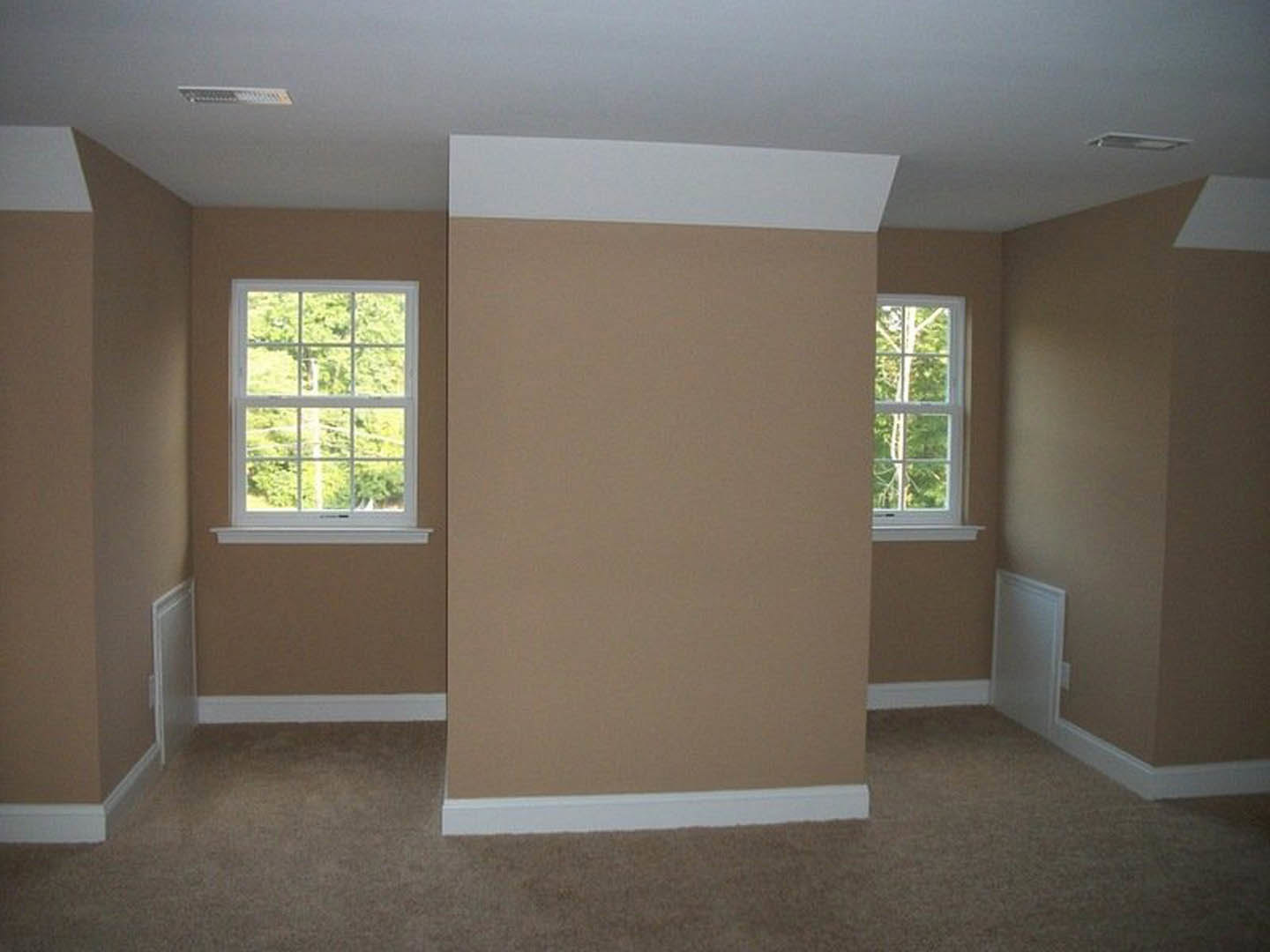 Beige-walled room with white trim, white-framed windows overlooking trees, light flooring, and plaster ceiling