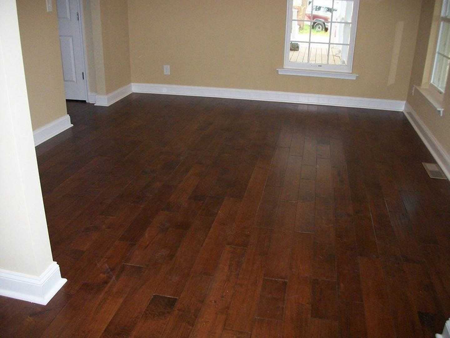 Dark hardwood floors in a room with white walls, white door, and window showing a parked car outside