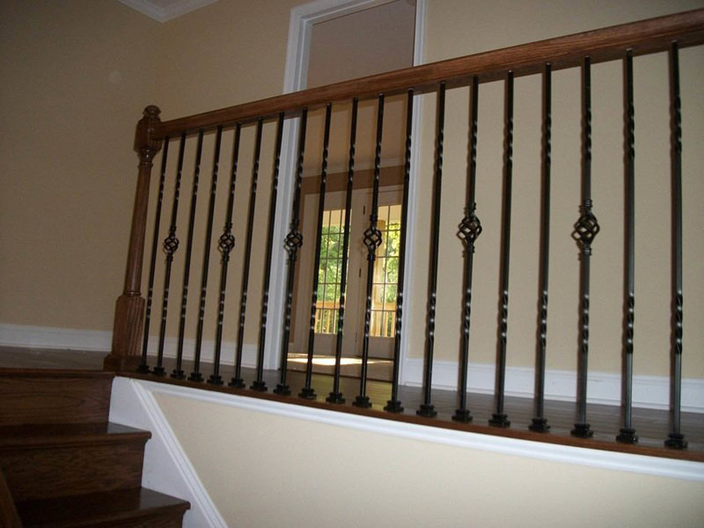 Wooden staircase with black metal railings against a white wall, featuring gold accents and a close-up view of the handrail and balusters.