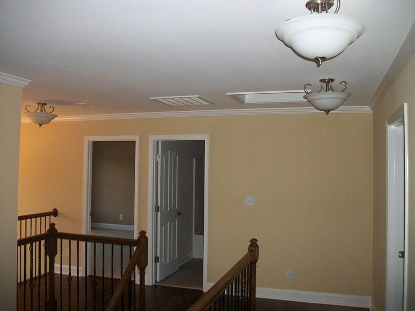 Hallway with white walls, crown molding, white door with silver handle, and ceiling-mounted light fixture with white shade
