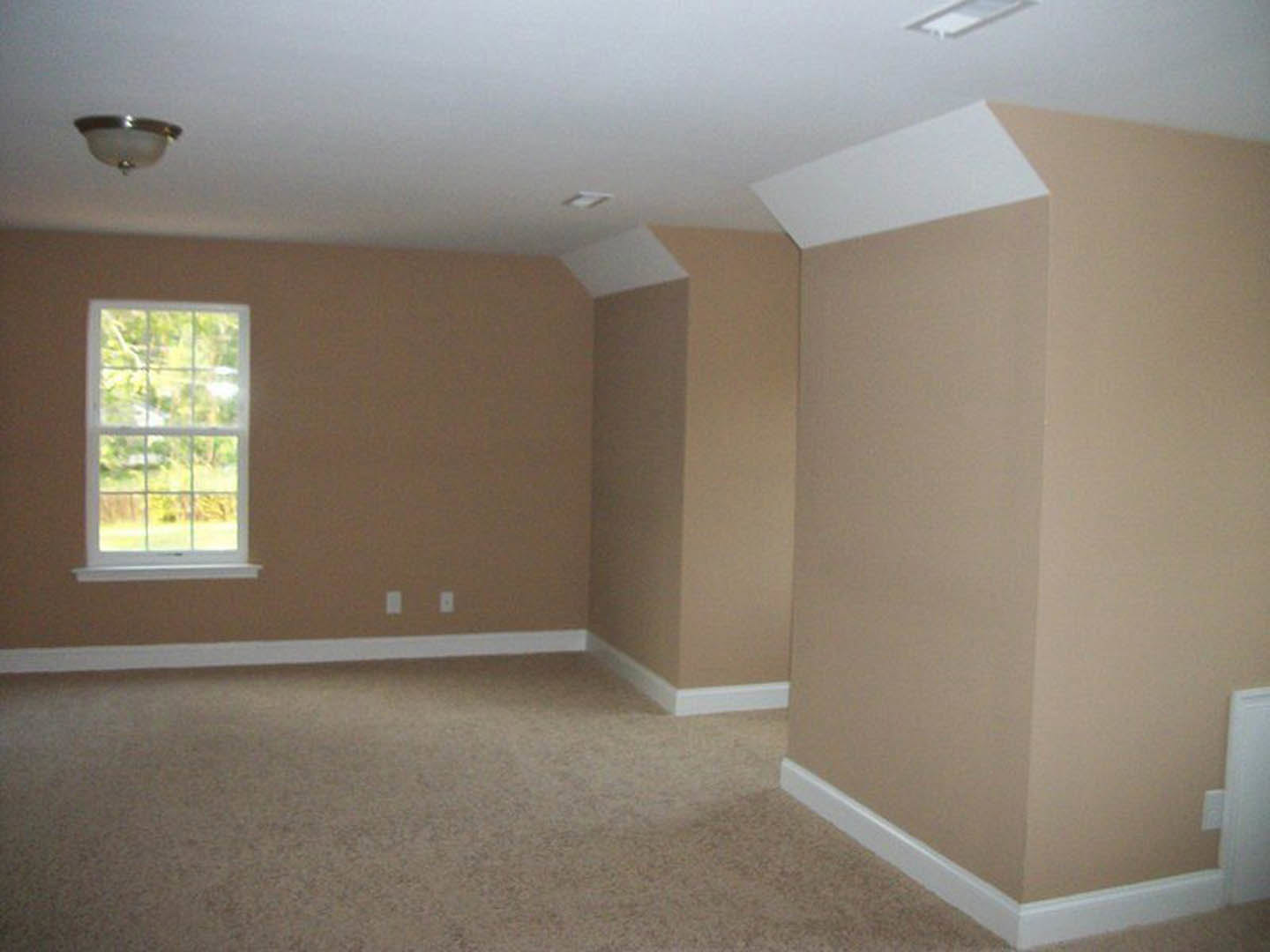 Carpeted room with beige walls, white trim, large window overlooking trees, and modern light fixture on ceiling