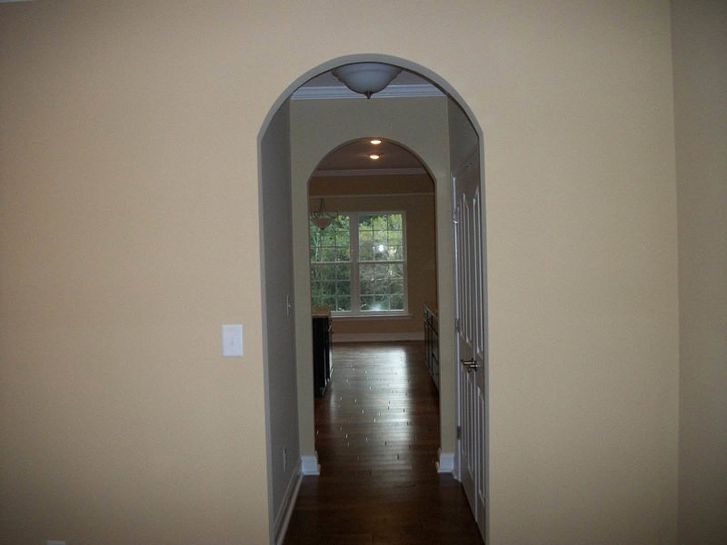 Hallway with dark wood flooring, white trim, a window, and a chandelier-style light fixture; white light switch visible on the wall