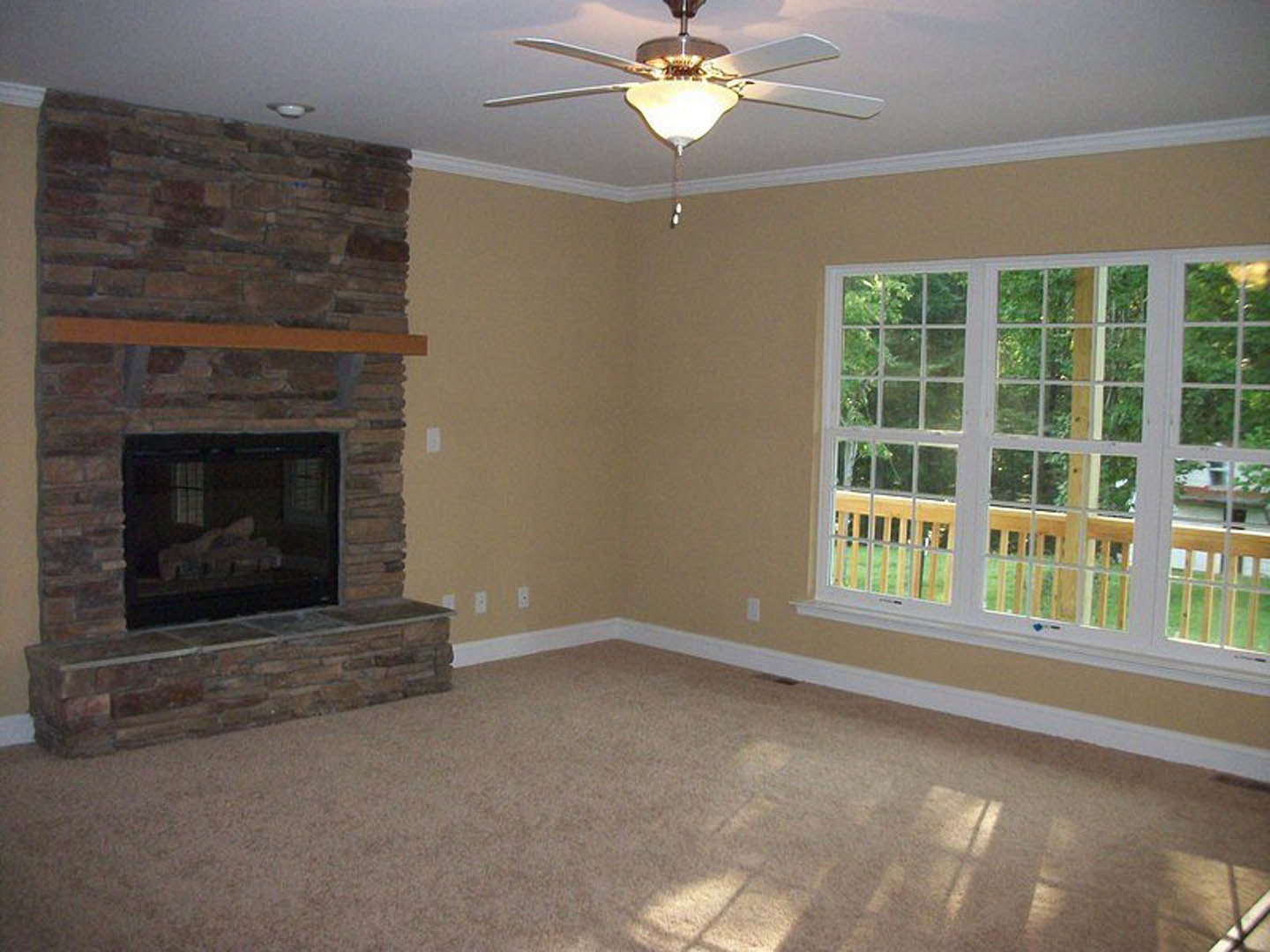 Living room with multi-pane window, wooden mantel fireplace burning logs, ceiling fan with light fixture, hardwood floors, and neutral walls
